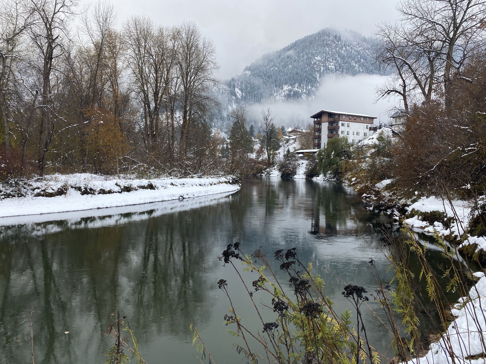 Snow-covered riverbanks and bare trees surround a calm river under a cloudy sky. - Barn Beach Pea Vine Trail