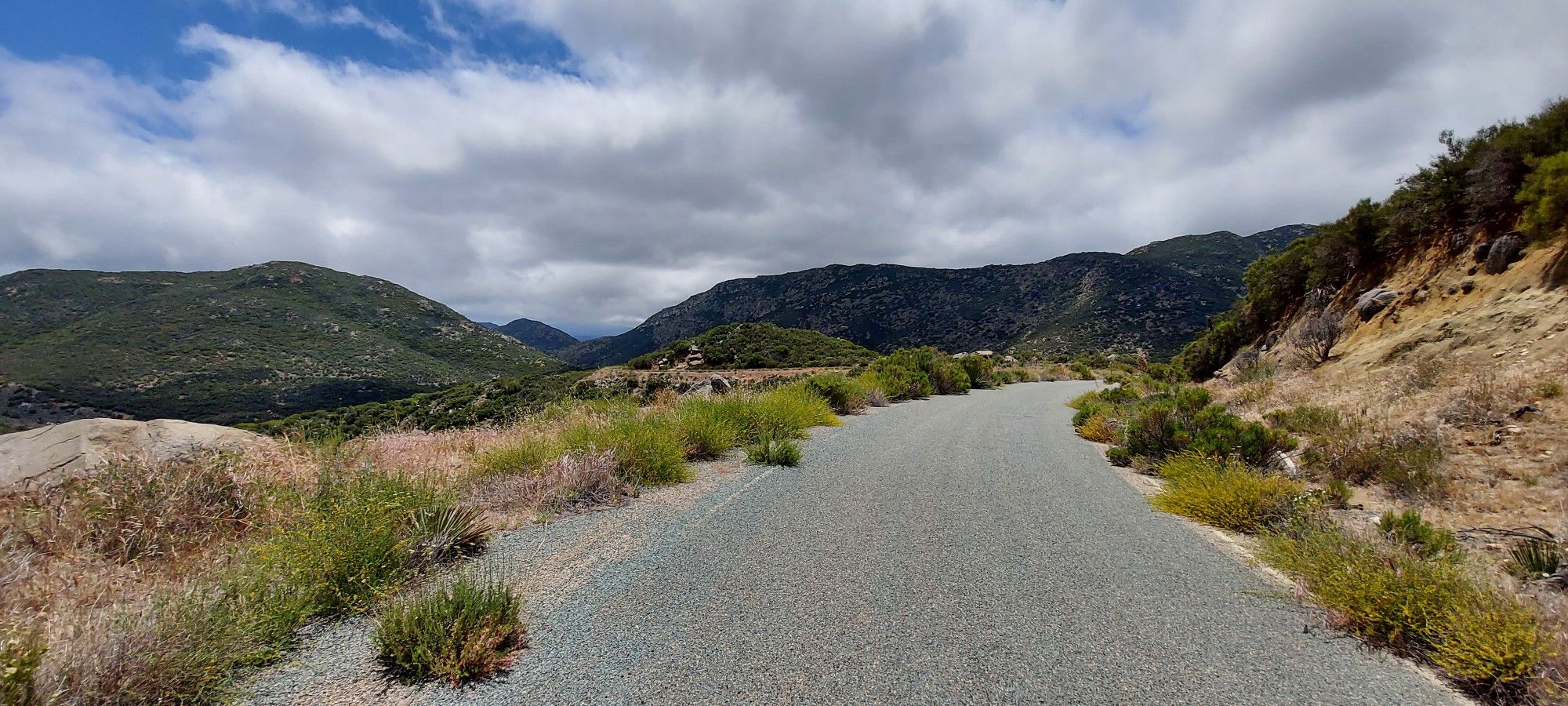 Paved road curving through green and dry hills under a cloudy sky. - Storm Canyon Overlook – Kwaaymii Point loop from Julian