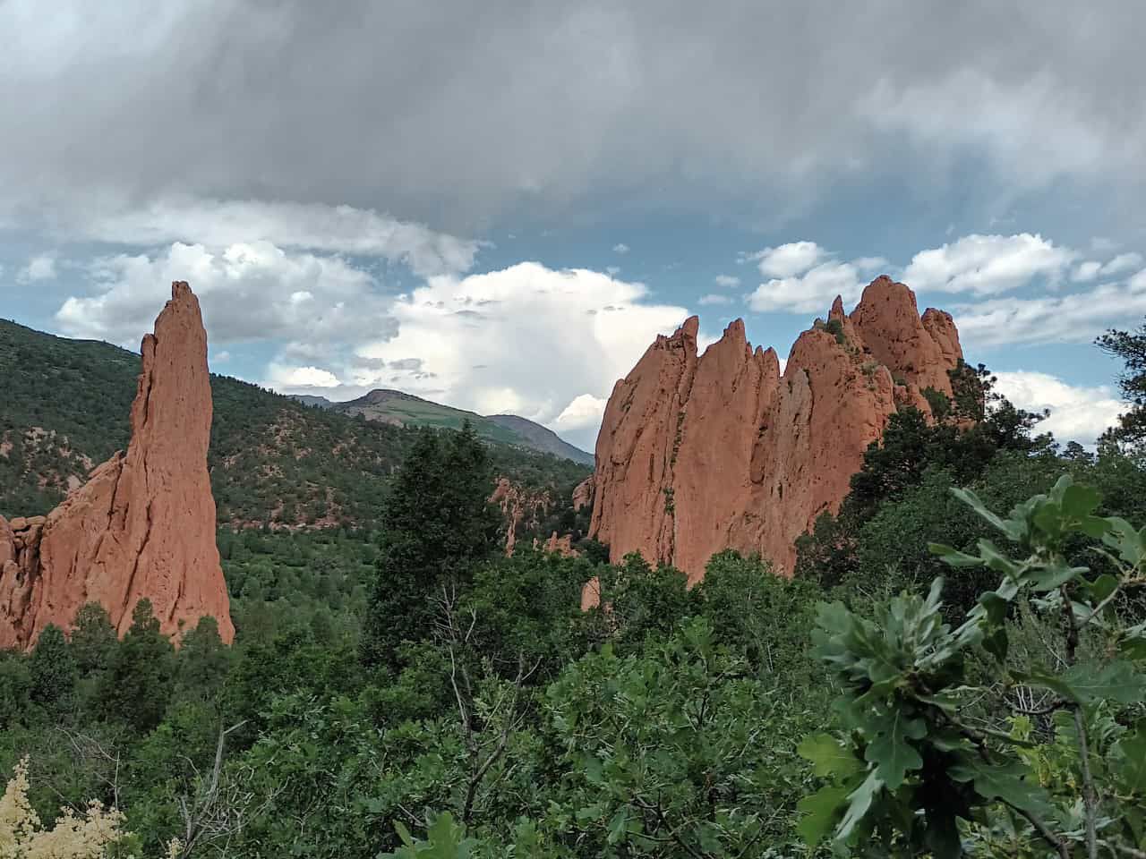 Towering red rock formations rise above green trees under a cloudy sky. - Colorado Front Range Trail and Pikes Peak Greenway Loop