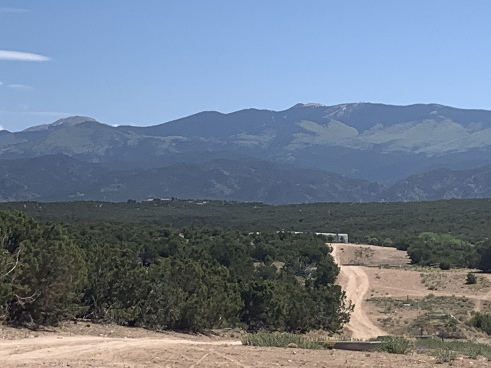 Distant mountains overlook a forested landscape with a winding dirt road. - La Tierra Trails Loop from Santa Fe