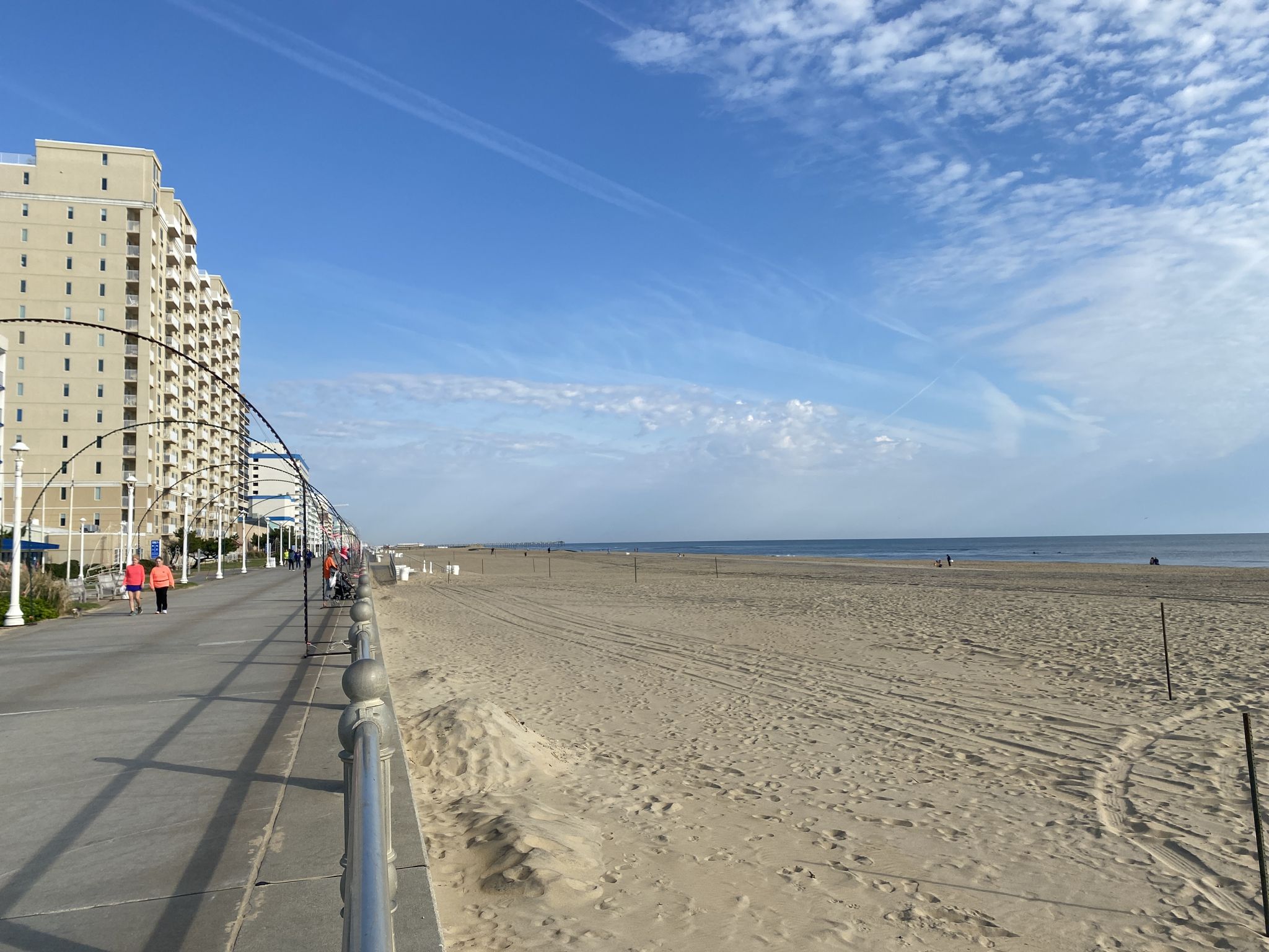 Wide sandy beach next to a boardwalk with tall buildings under a blue sky. - King Neptune Statue – Virginia Beach loop from JEB Little Creek – Fort Story 67th Street Cottages