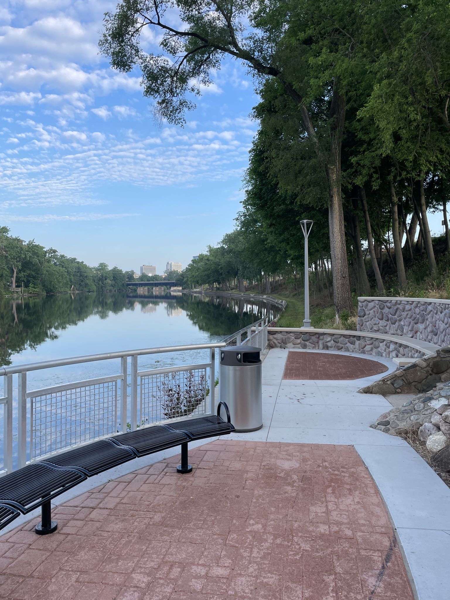 Modern park area with a bench and railing next to a calm river. - East Race Waterway – Basilica of the Sacred Heart loop from University of Notre Dame du Lac