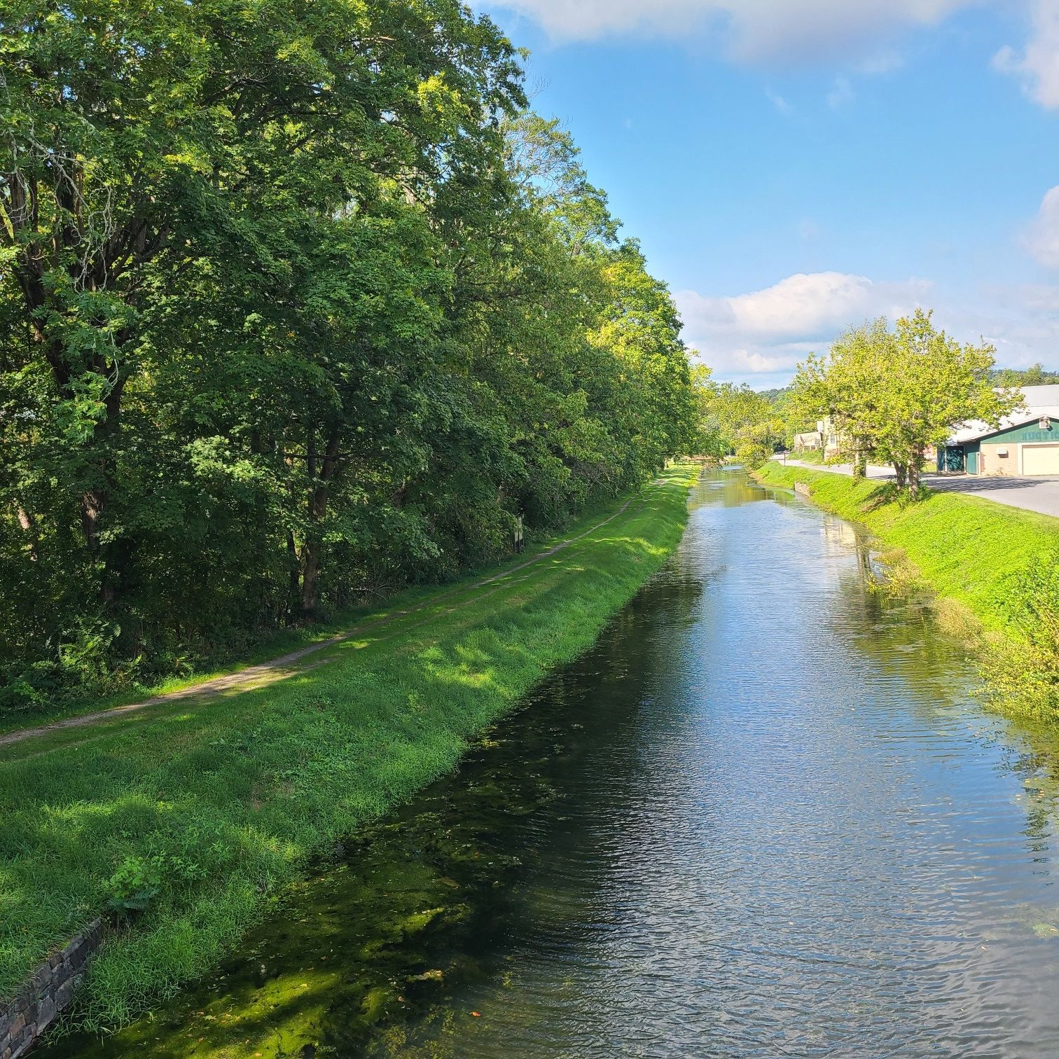 A calm canal flows between green banks under a bright blue sky. - Town of Hancock loop from Fort Frederick State Park