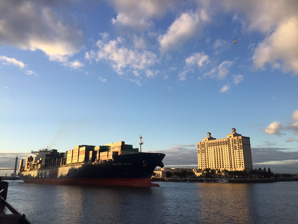 Container ship on a river, passing a large building at sunset. - City Market, Savannah – Wright Square loop from Savannah