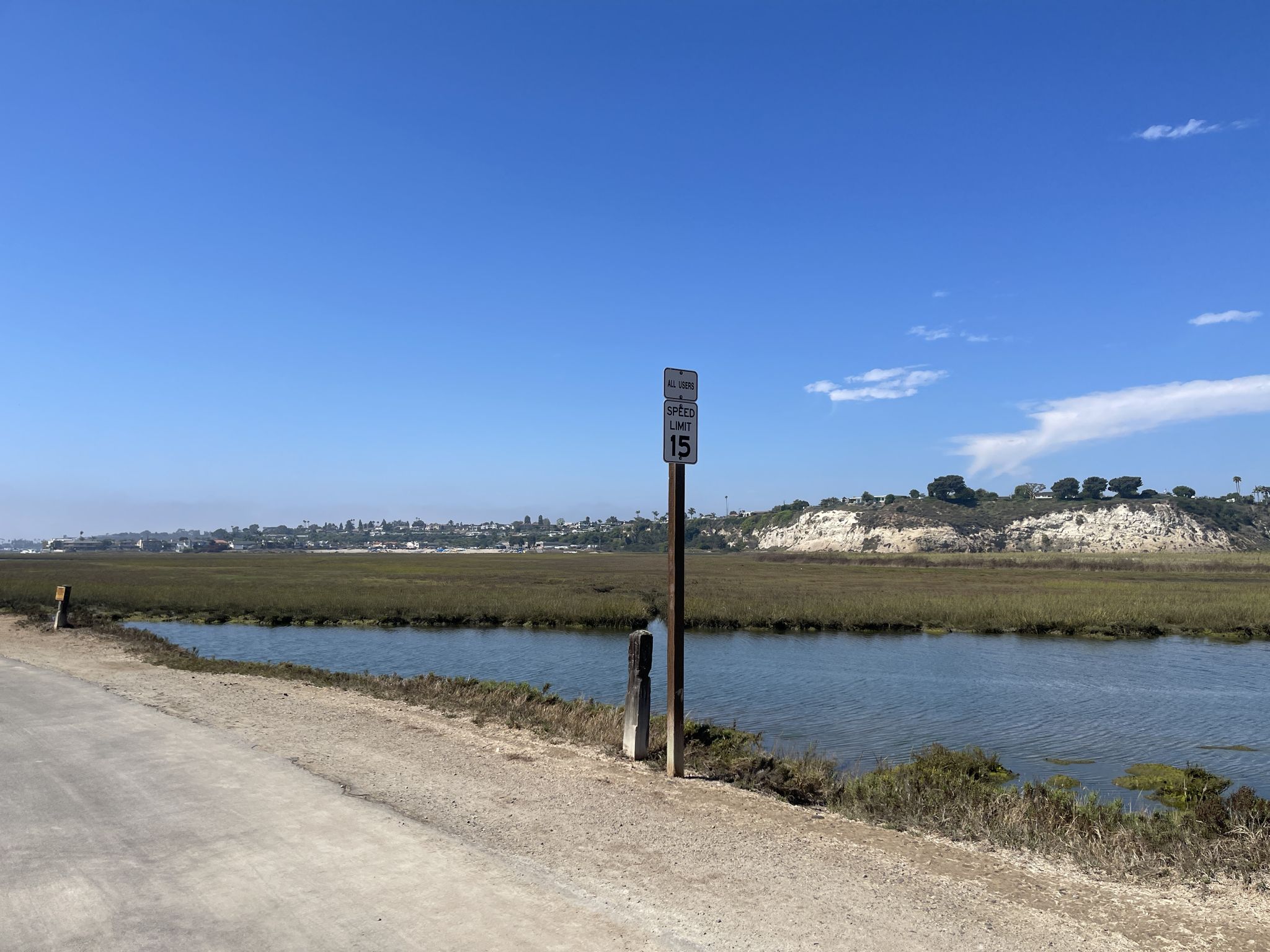 A speed limit sign next to a road, overlooking a wetland and distant hills. - Back Bay Loop Trail