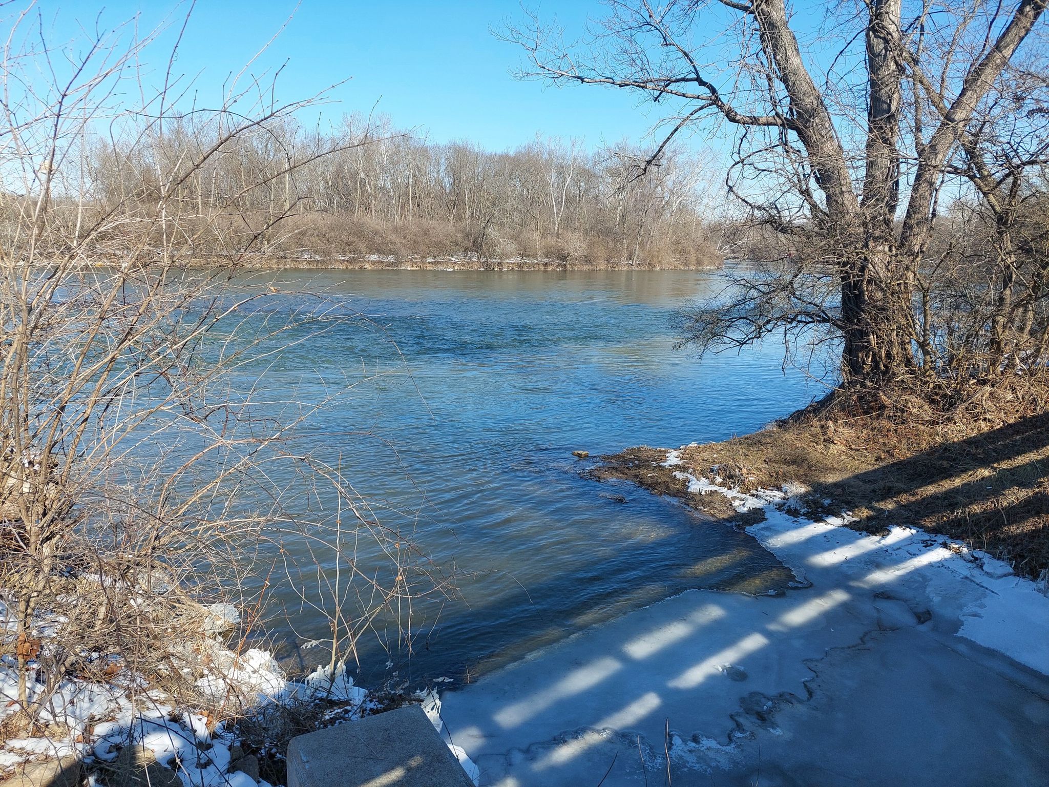 Blue river water with bare trees, snow on banks, and a concrete ramp. - Hutchins State Reservoir loop from Chautauqua