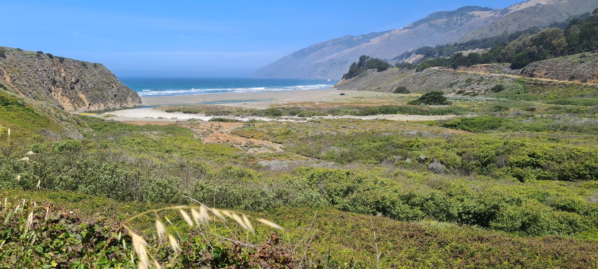 Sunny coastal landscape with a sandy beach, ocean, and green mountains. - Ragged Point via Coast Highway