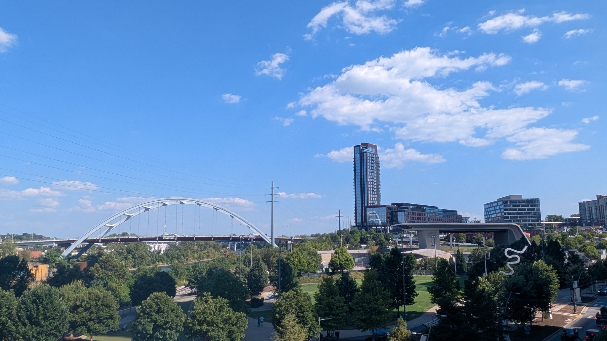 Arch bridge and tall building in a city park, blue sky. - Nashville Riverfront – Tennessee State Capitol Hill loop from Riverfront