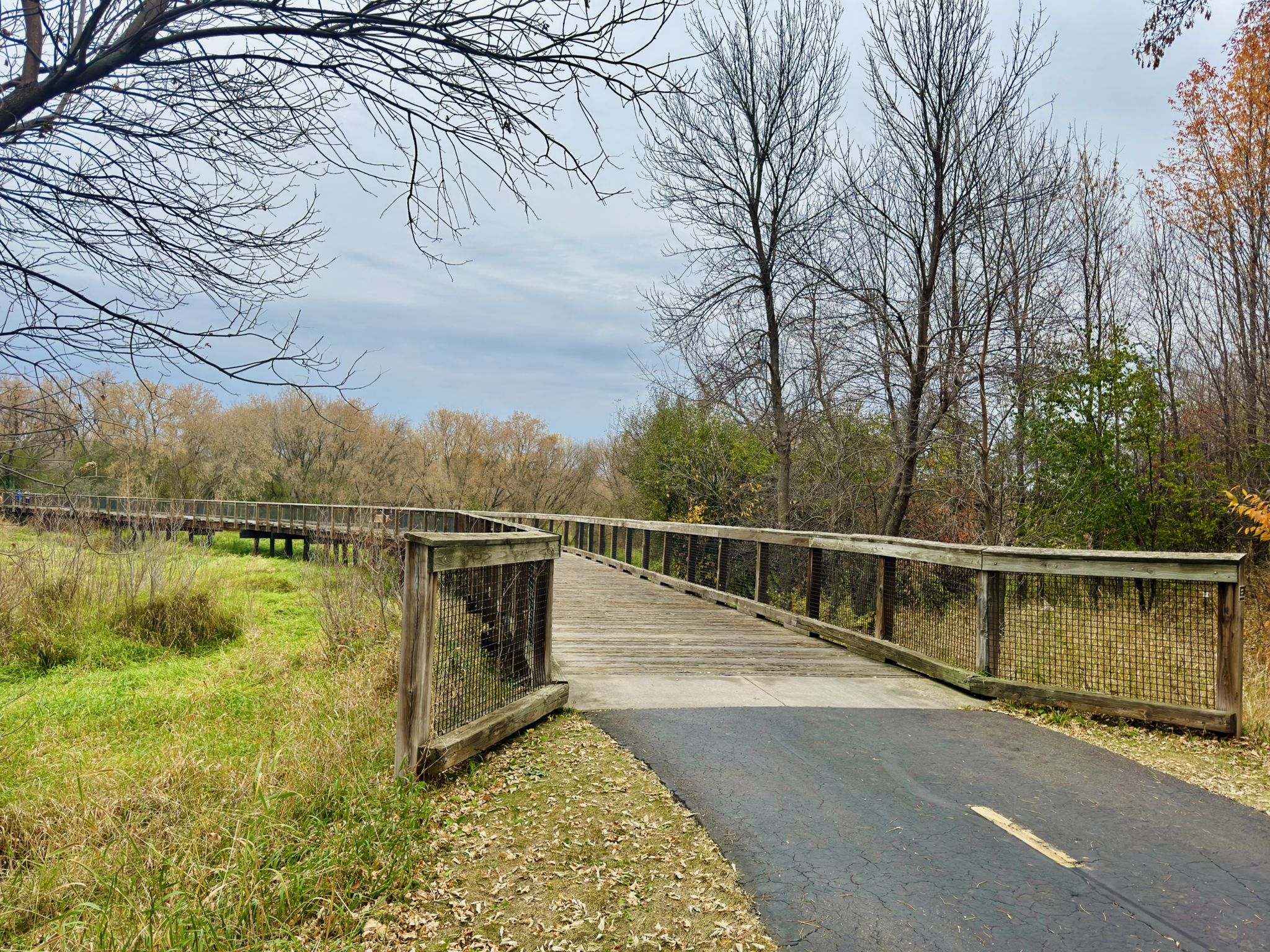 Wooden boardwalk and paved path through autumn trees under a cloudy sky. - Valley Trail – Elm Creek Park Trailhead loop from Elm Creek