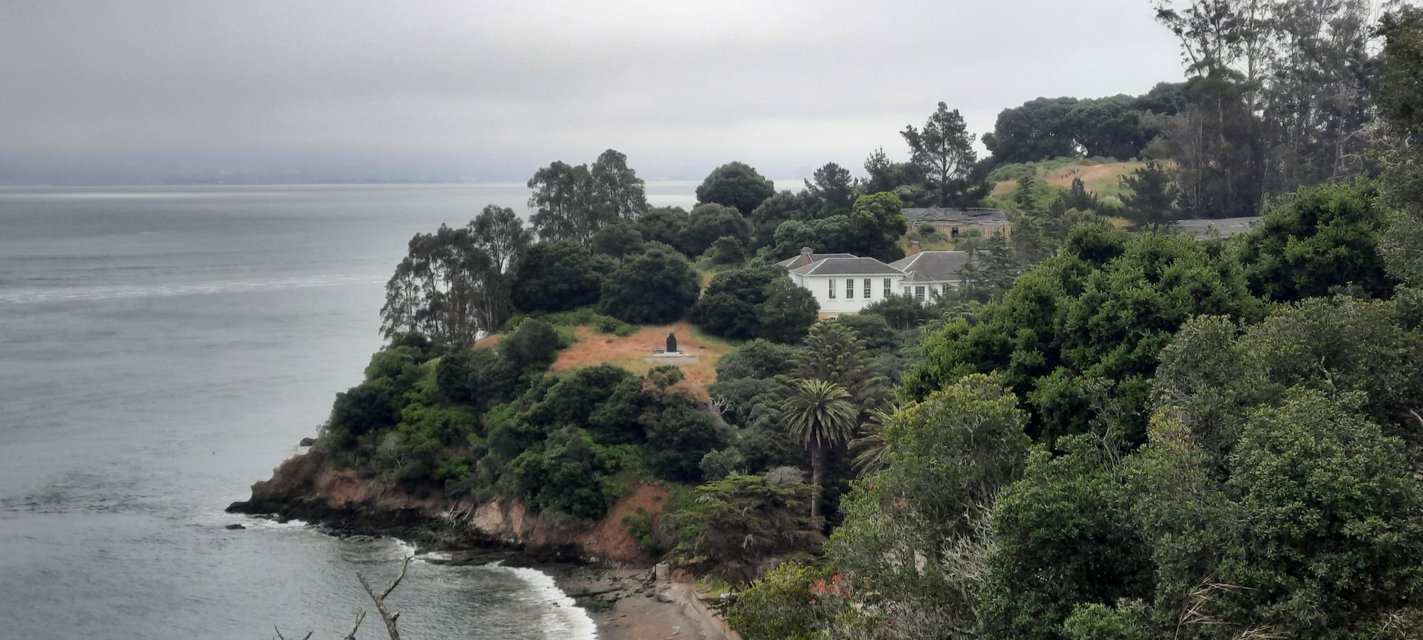 Overcast view of a white building nestled among dense trees by the coast. - Post Chapel, Fort McDowell – Quarry Beach loop from Angel Island