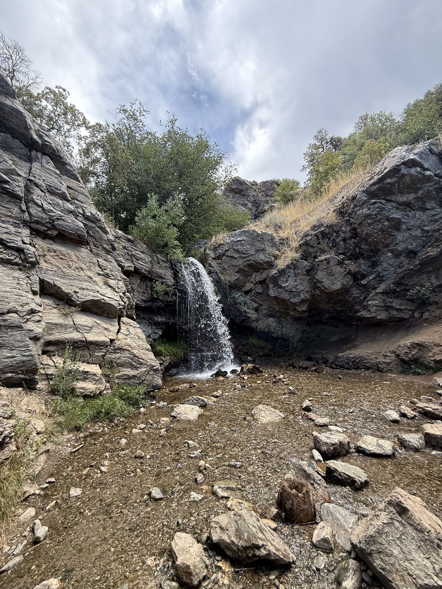 Waterfall flowing into a rocky stream bed under an overcast sky. - Adam’s Canyon Lower Falls