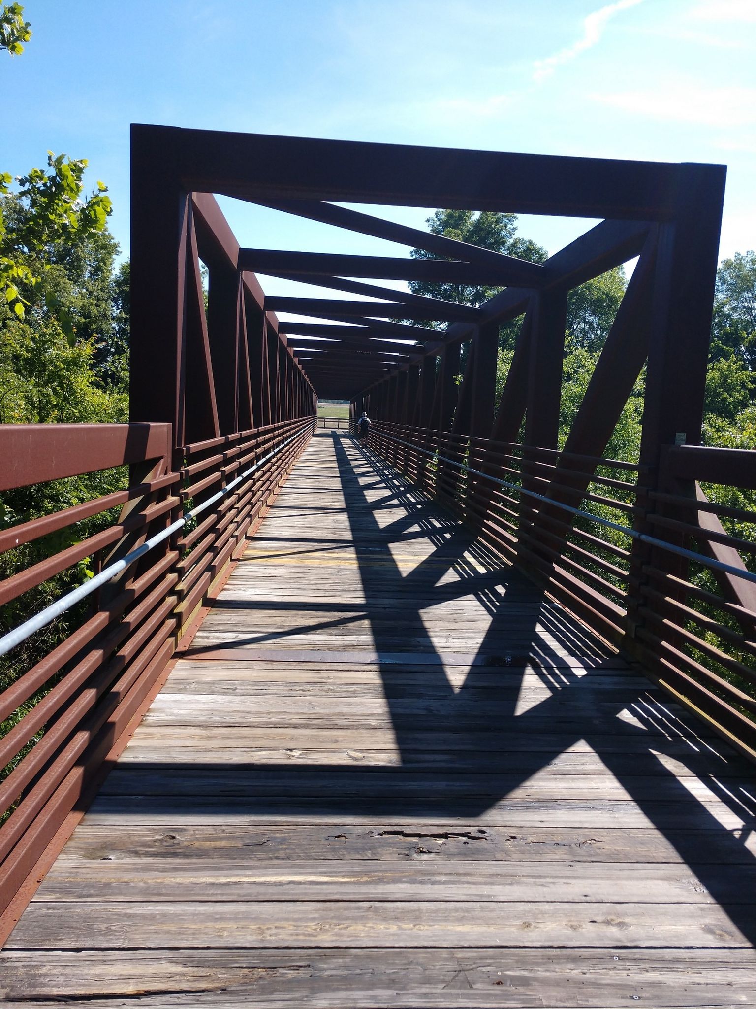 Long metal truss bridge with wooden deck, casting strong shadows on a sunny day. - Neuse River Trail to Williamson Preserve