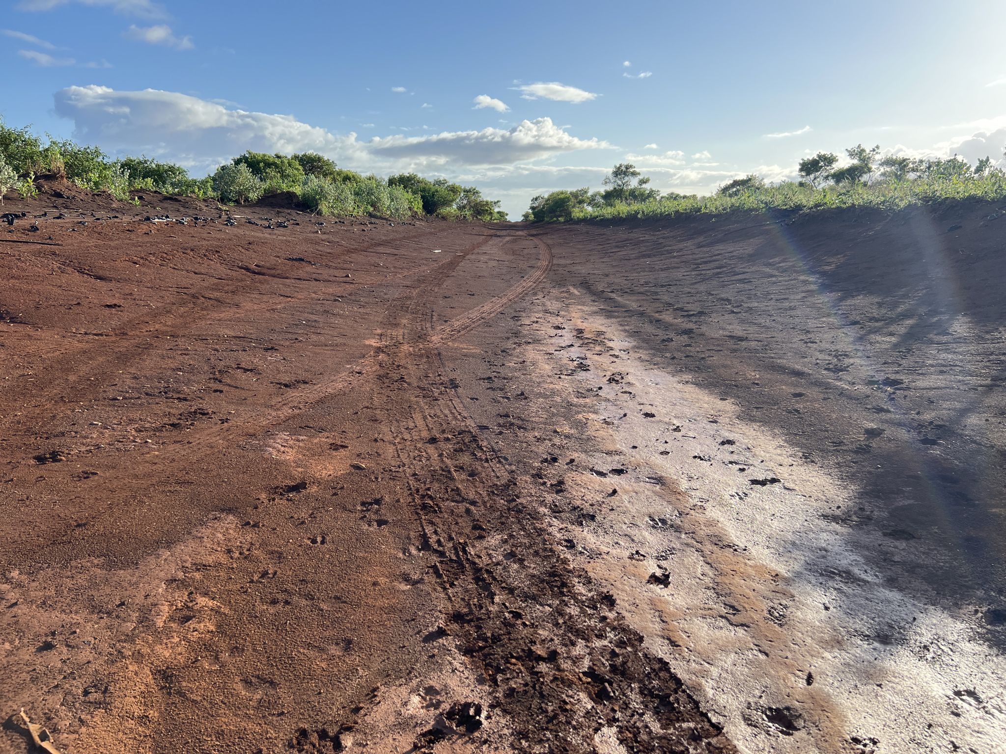 Wide red dirt path with tire tracks under a bright, cloudy sky. - Munro Trail