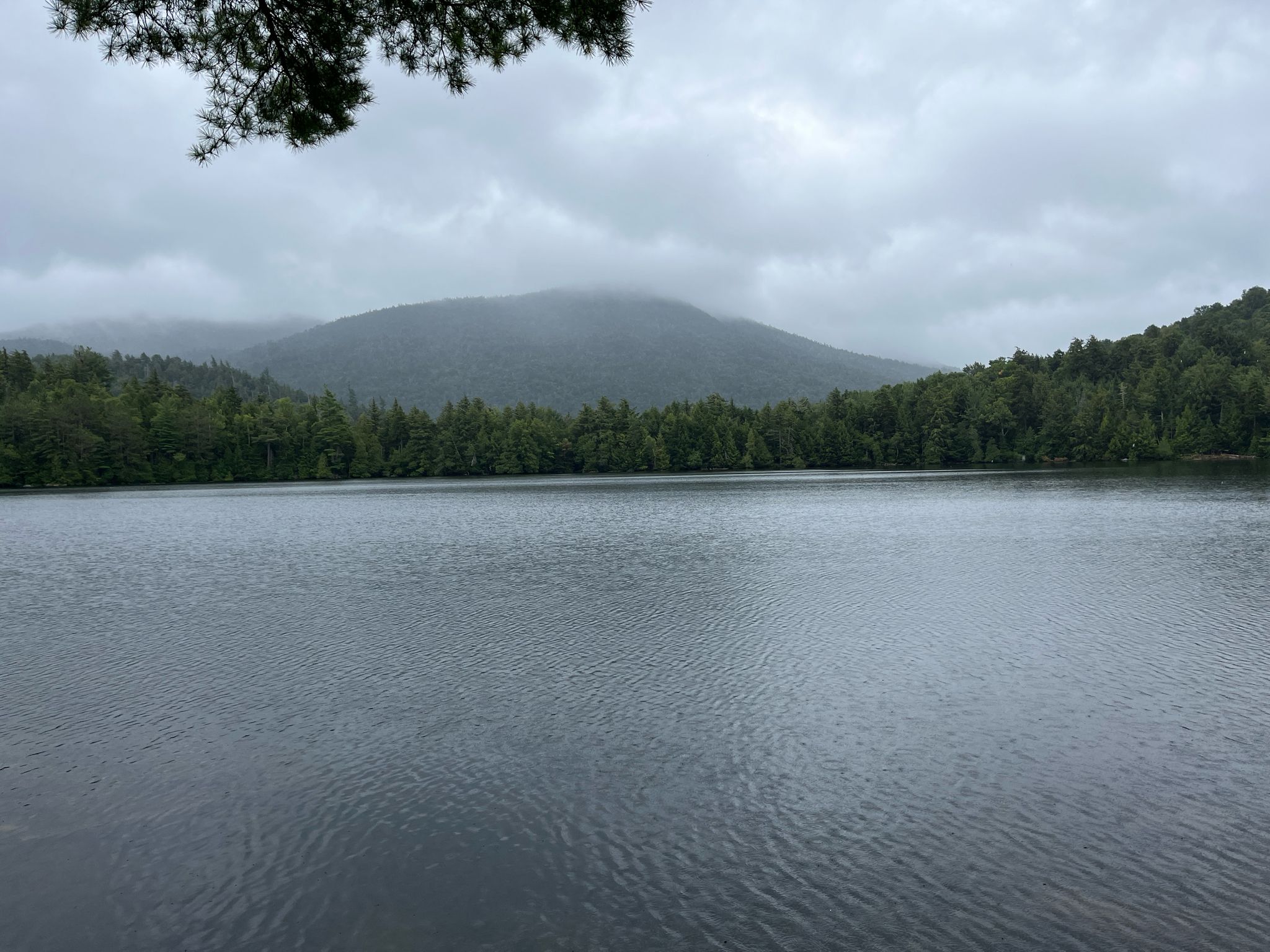 A calm lake with forested mountains under an overcast sky. - Copperas Pond Trail