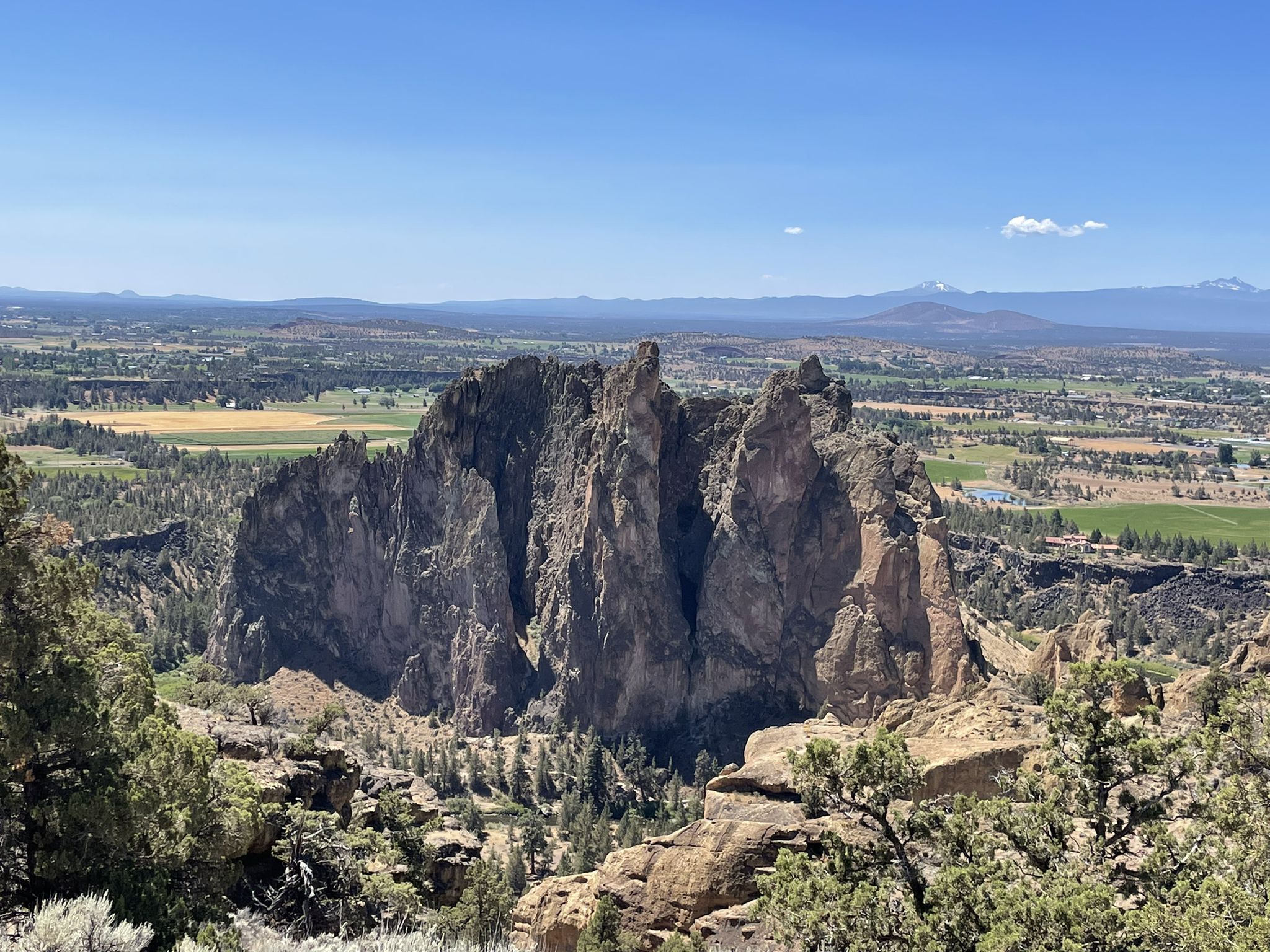 Majestic rock formations overlook a green valley under a clear blue sky. - Misery Ridge Trail