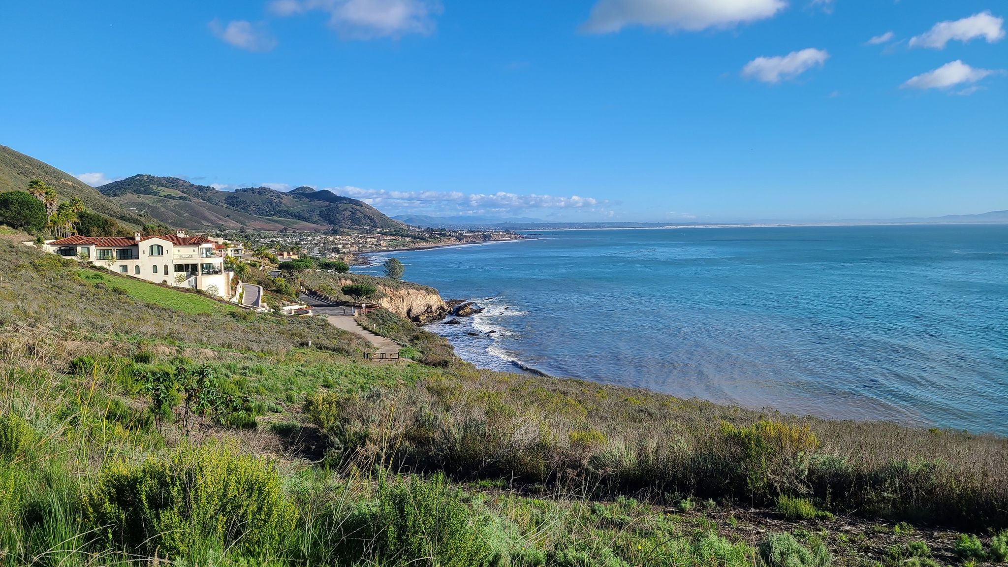 Bright coastal view with a large house on a hillside overlooking the ocean. - Ontario Ridge Trail loop from Avila Beach
