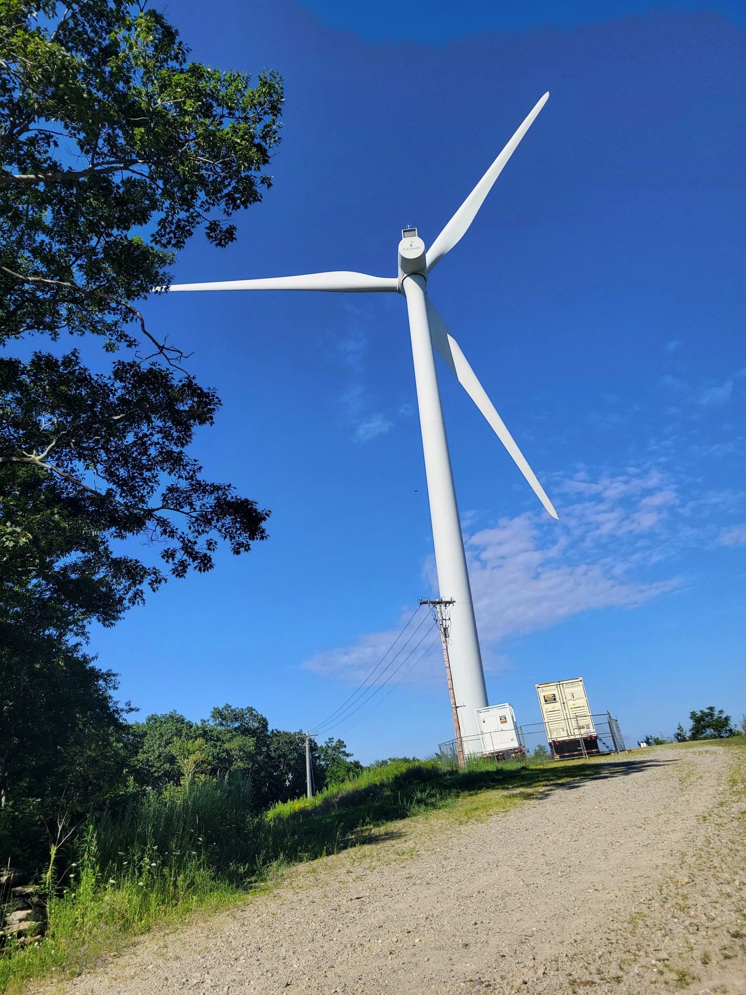 Large white wind turbine next to a dirt road under a bright blue sky. - Wachusett Mountain Old Indian, Stage Coach, Bicentennial Trails
