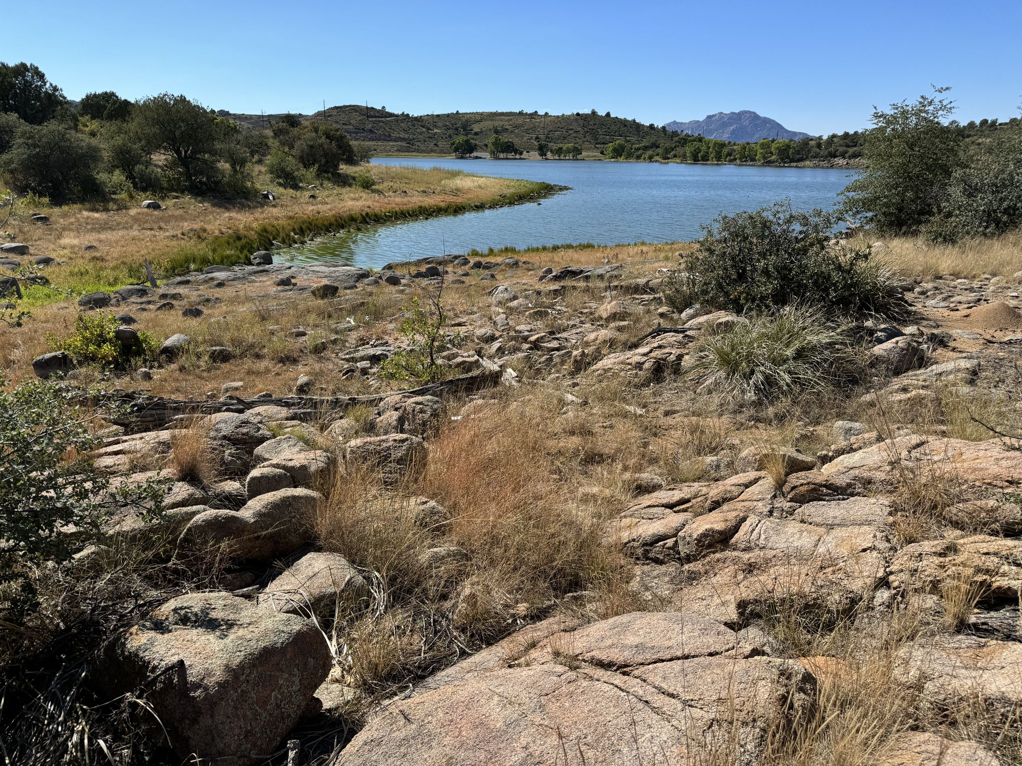 Sunny view of a lake bordered by rocky, dry terrain and distant hills. - Watson Lake Loop Trail