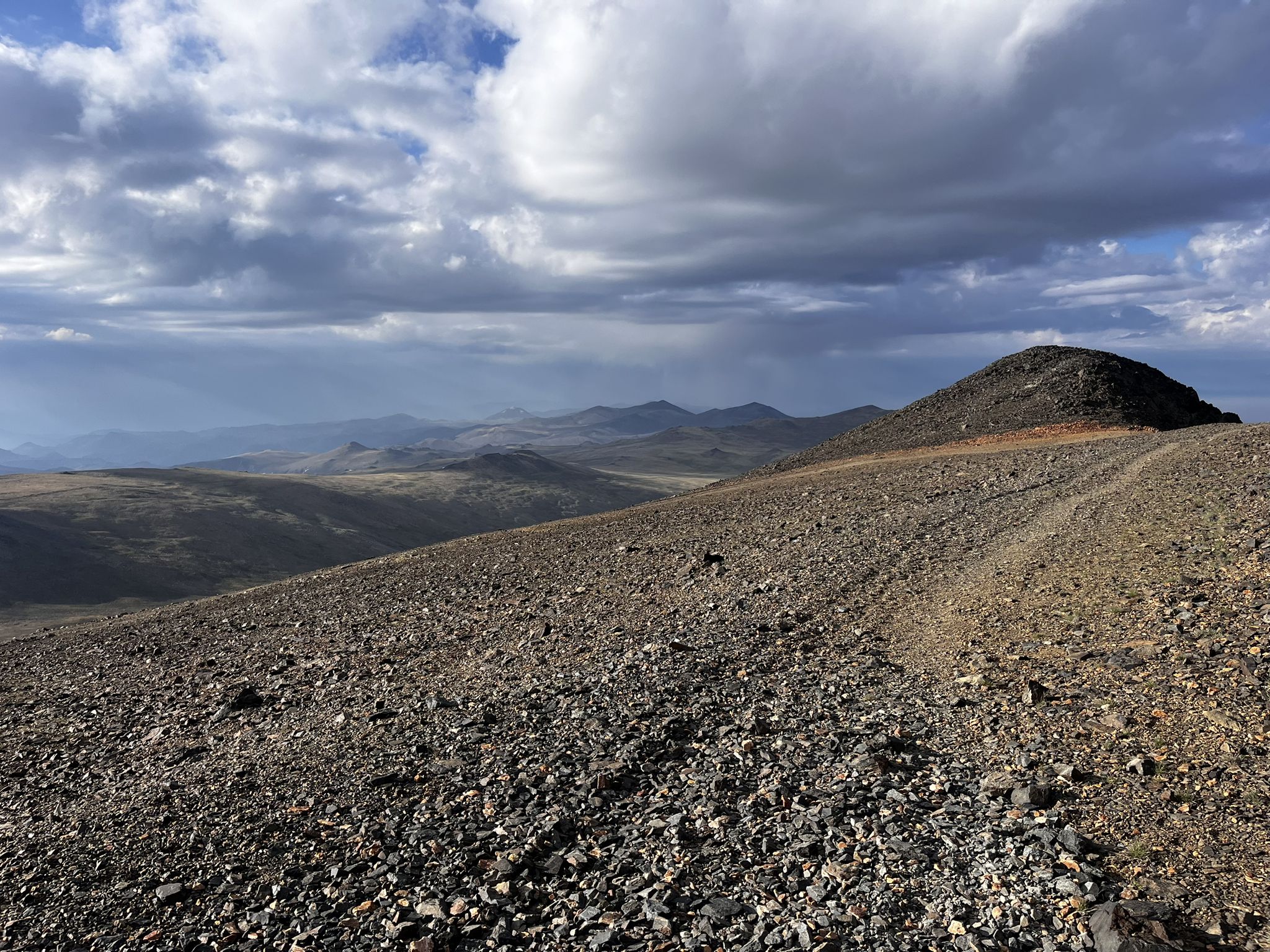 Rocky, barren landscape with a dirt road under a cloudy sky. - White Mountain Peak Trail