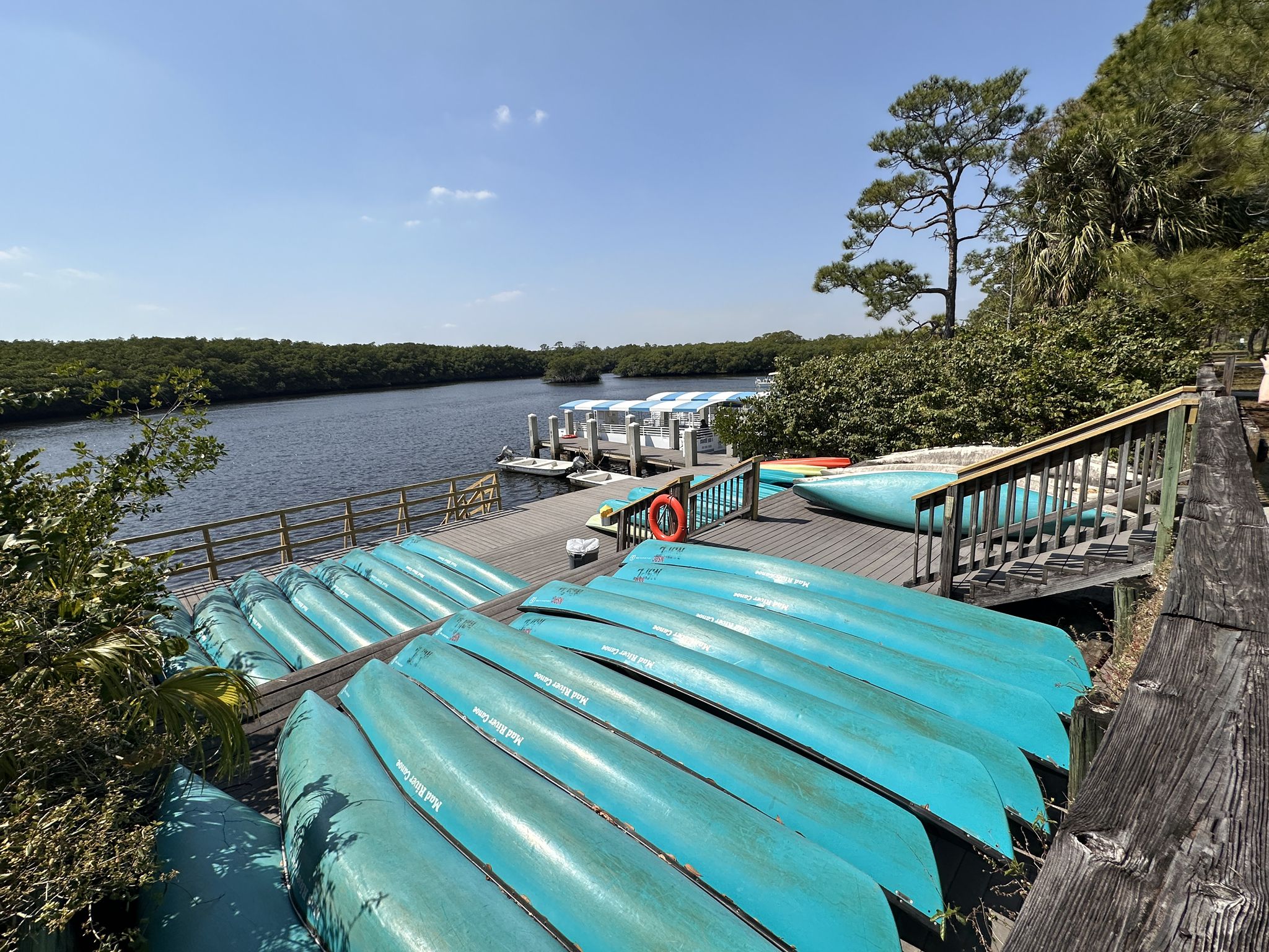 Stacked blue kayaks and canoes on a wooden deck next to a river dock. - Visitor Center – Tour Boat Dock loop from Jonathan Dickinson State Park