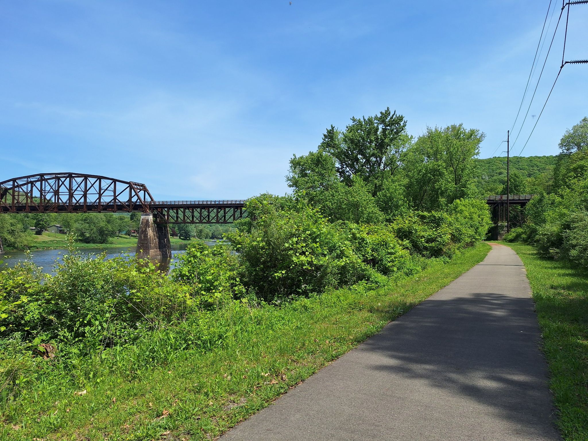 Paved path alongside a river with a large metal bridge on a sunny day. - Indian God Rock – Rockland Furnace loop from Cranberry Township