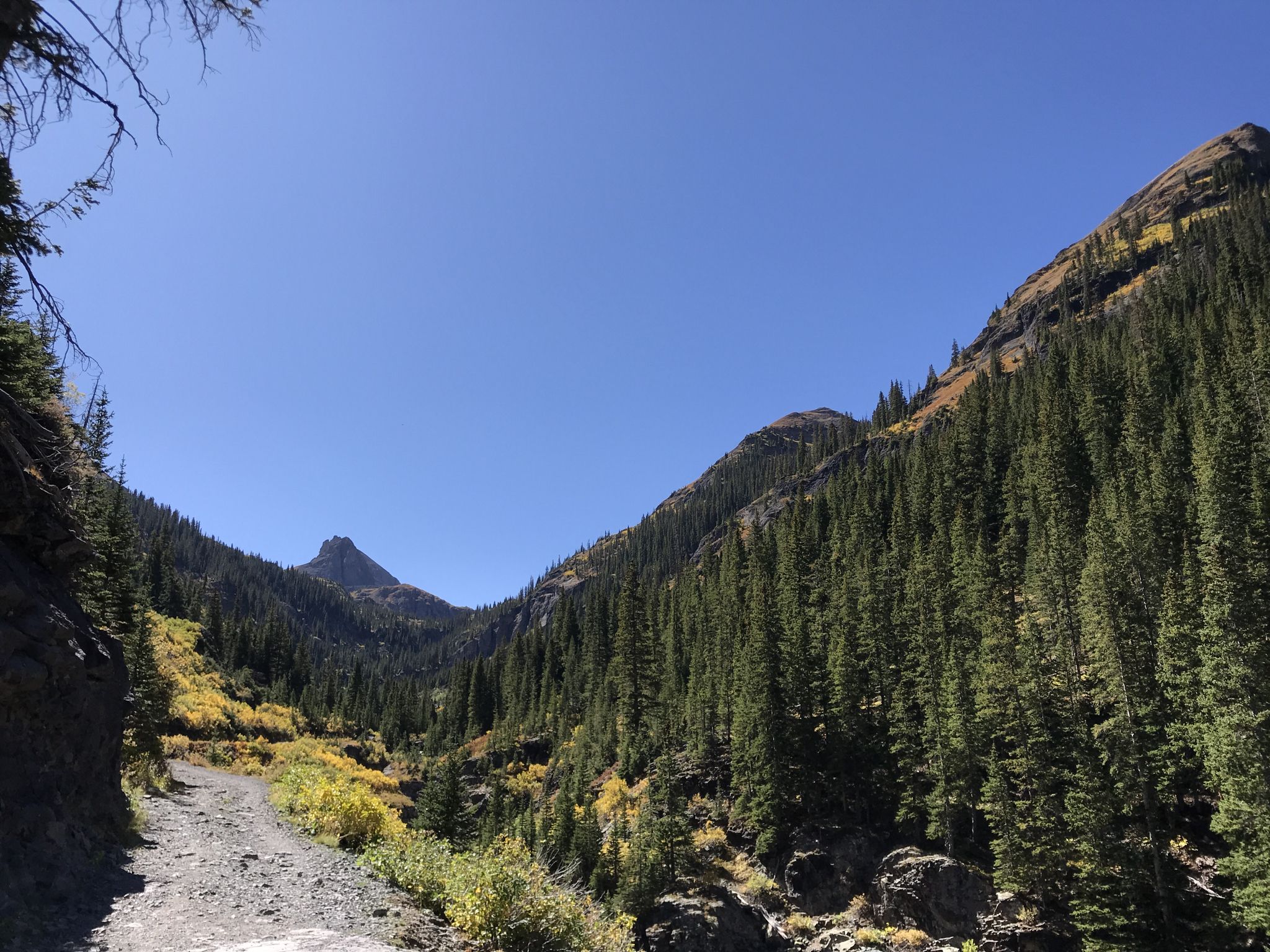 Dirt road winding through a forested mountain valley with clear blue sky. - Bridal Veil Falls to Silver Lake Trail