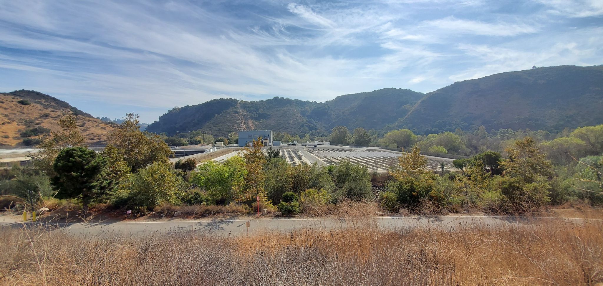 A large industrial facility with solar panels nestled in a valley between green hills. - Canejo Canyon Open Space Loop