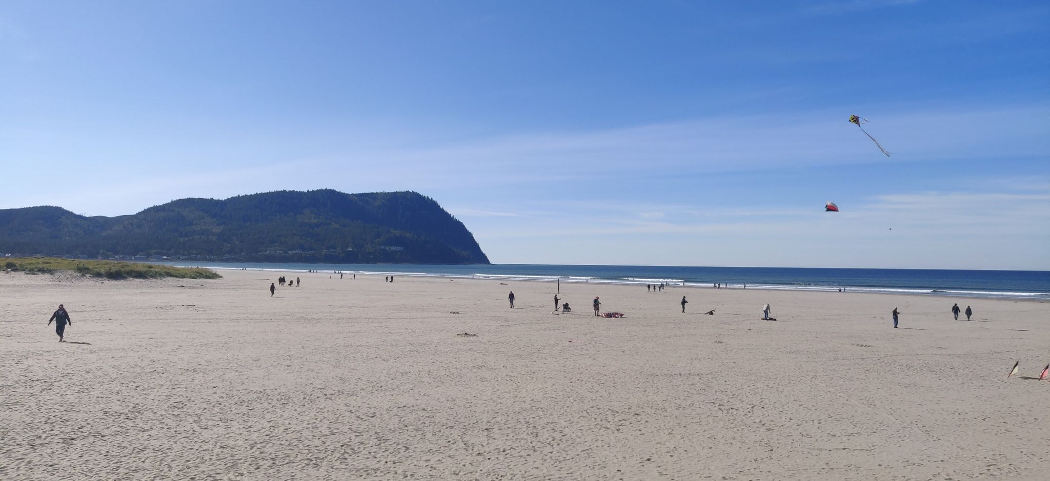 People walk on a wide sandy beach with ocean waves and a large mountain. - Seaside Cove and Seltzer Park loop from Seaside