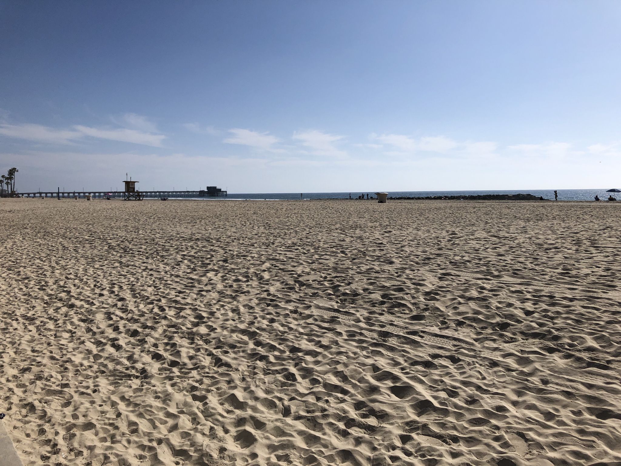 Wide sandy beach with a distant pier and lifeguard tower under a clear sky. - Balboa Peninsula from Newport Beach