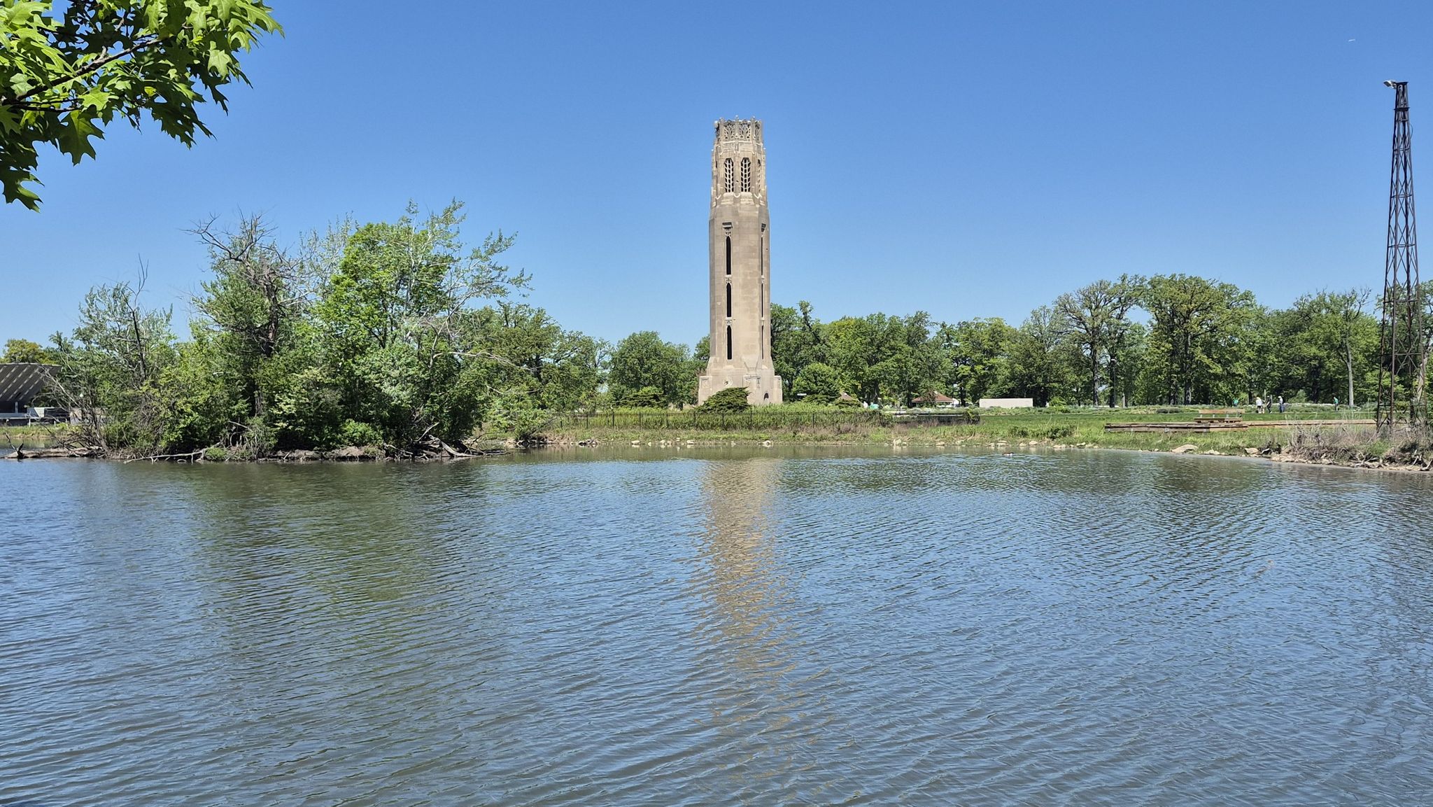 Tall stone tower beyond calm water and green trees on a sunny day. - Bald Eagle on Belle Isle – Blue Heron Lagoon loop from Troy
