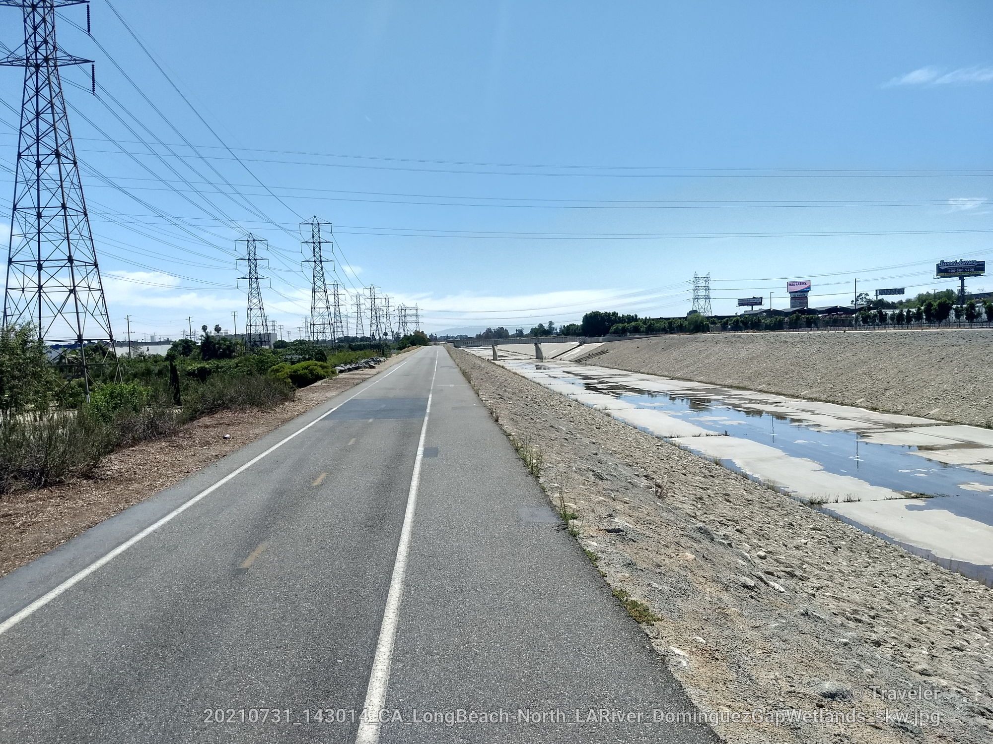 Long paved road next to a dry concrete channel with power lines. - Los Angeles River Loop