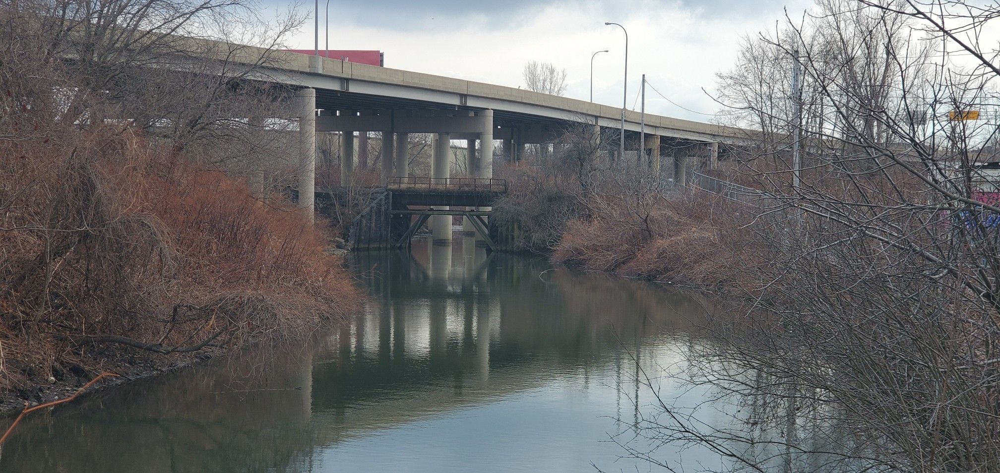Dark river flows under a concrete highway bridge on an overcast day. - Jesse Kregel Pathway