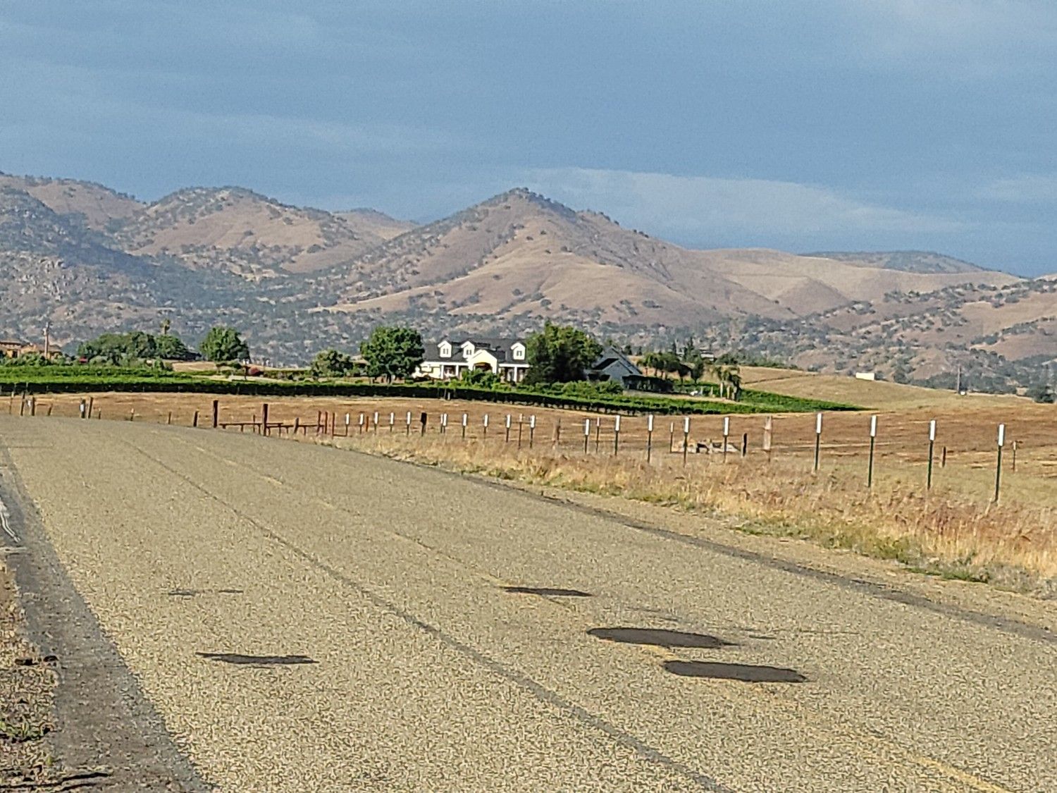 A paved road leads towards a house in dry fields with rolling mountains behind. - Fresno to Pine Flat Lake