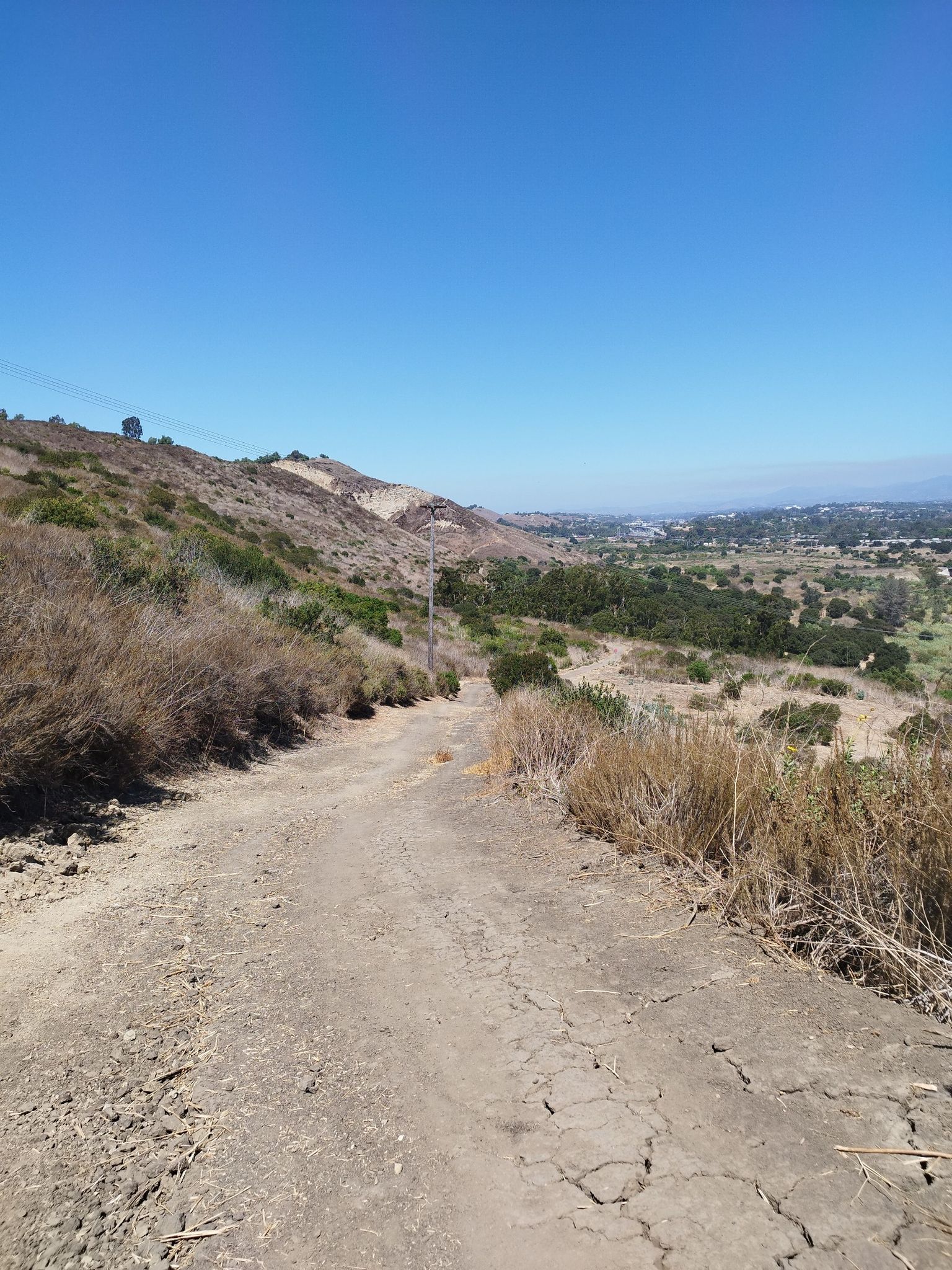 A dirt path descends a dry, brushy hillside under a clear blue sky. - Colinas Ridge and Shea Trail Loop