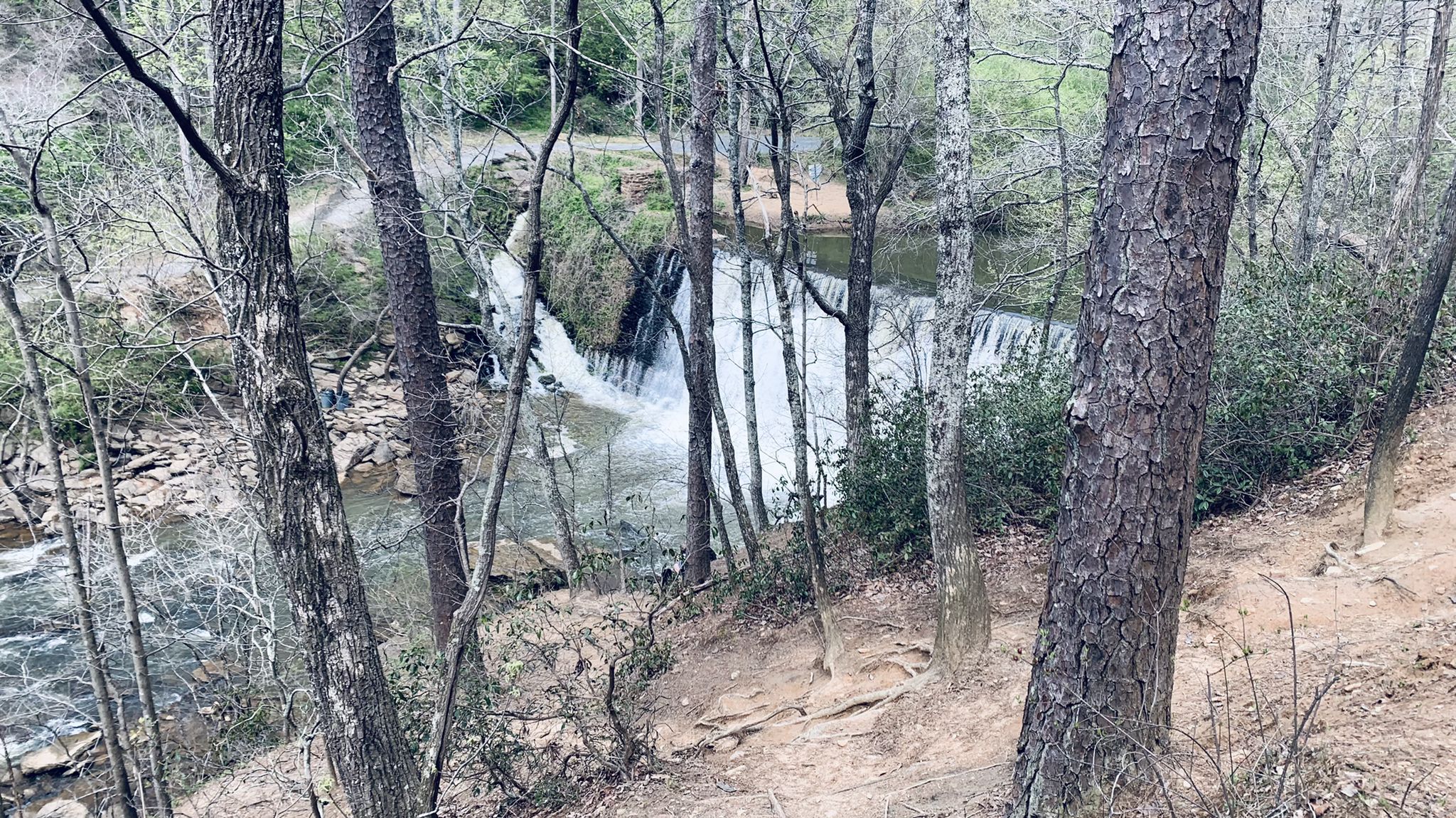A distant waterfall and river are visible through a sparse, wooded area. - Vickery Creek Trail Loop