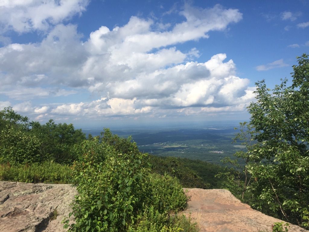 A wide mountain vista with green trees, rocky foreground, and cloudy blue sky. - Inspiration Point – Newman's Ledge loop from North Lake