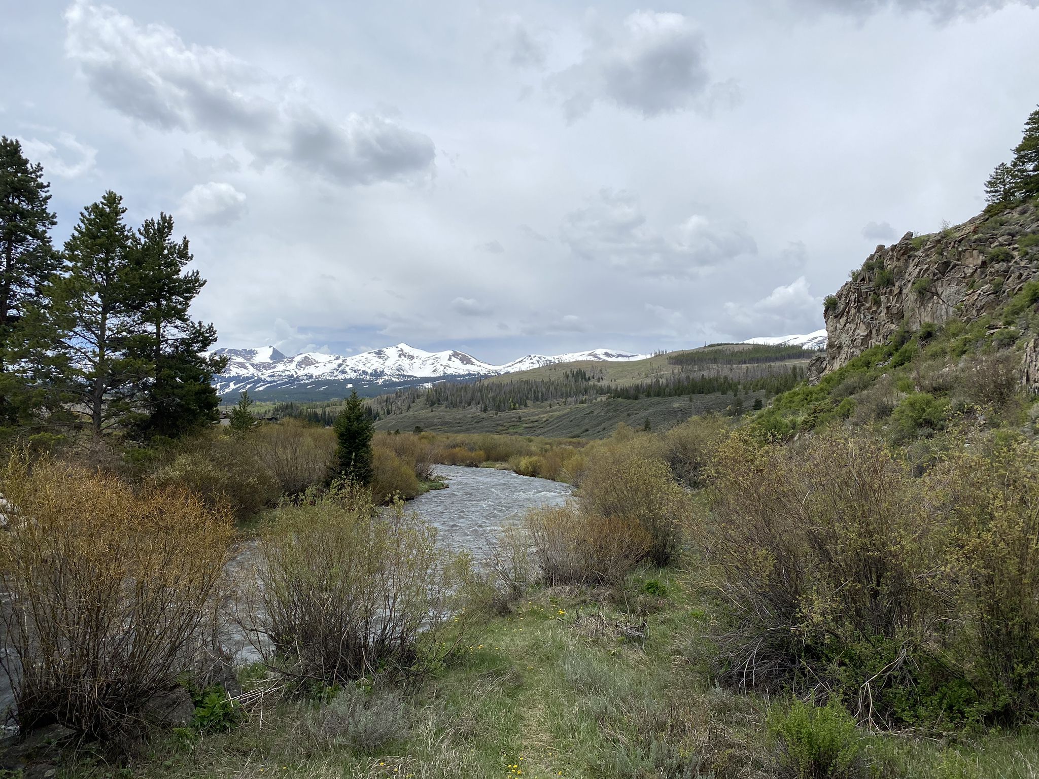 A winding river flows through a valley with bushes and snow-capped mountains. - Upper Blue Recpath