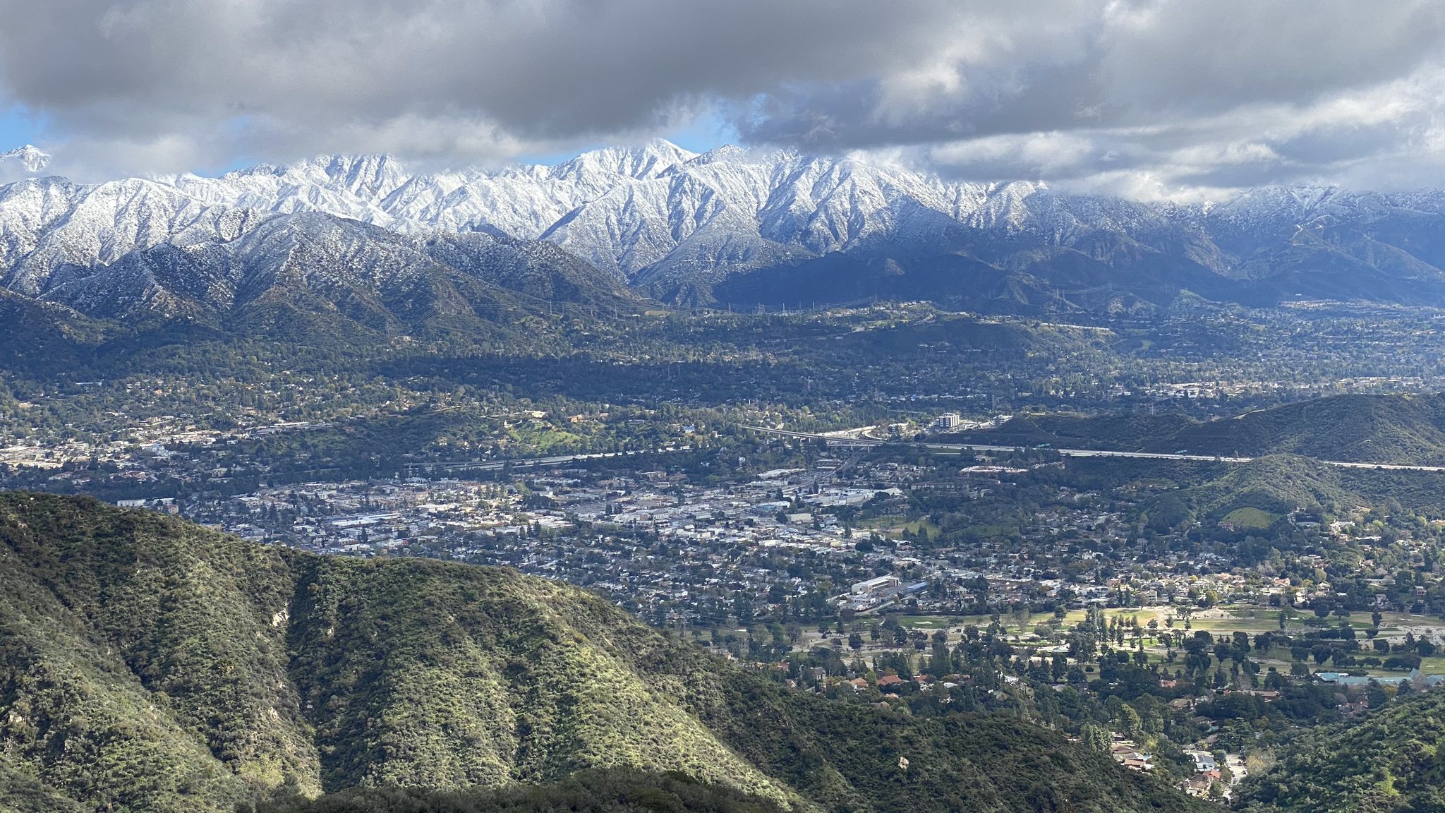 Cityscape nestled below snow-capped mountains under a partly cloudy sky. - Beaudry Motorway Loop