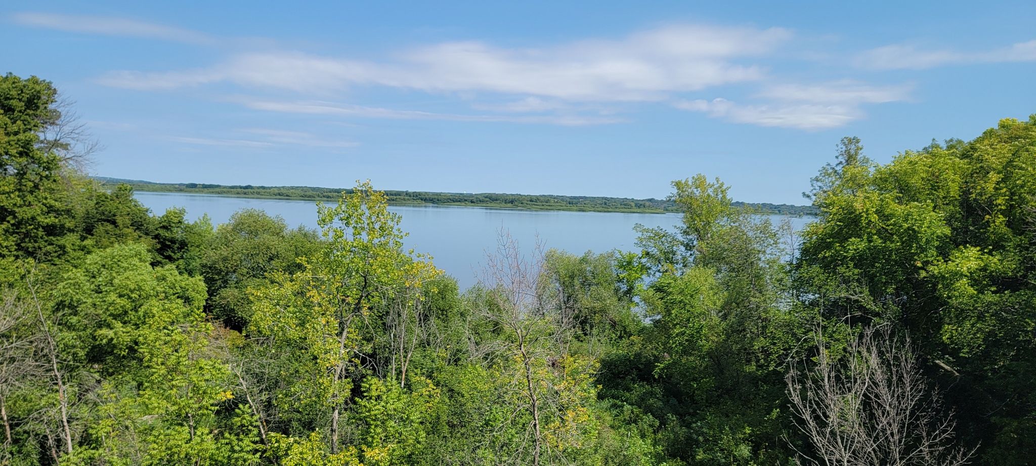 A wide river seen through lush green trees under a bright blue sky. - Mississippi River Greenway Loop