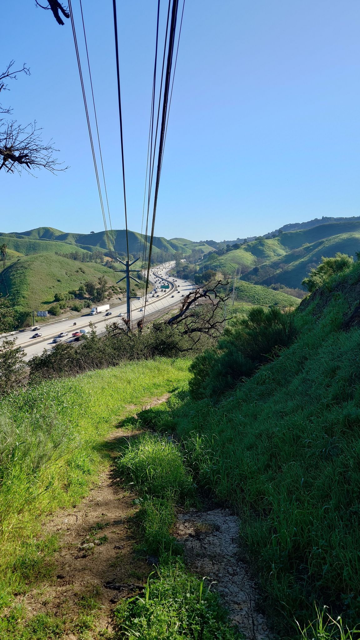 Overhead power lines above a busy highway winding through green hills. - New Millennium and Anza Loop Trail