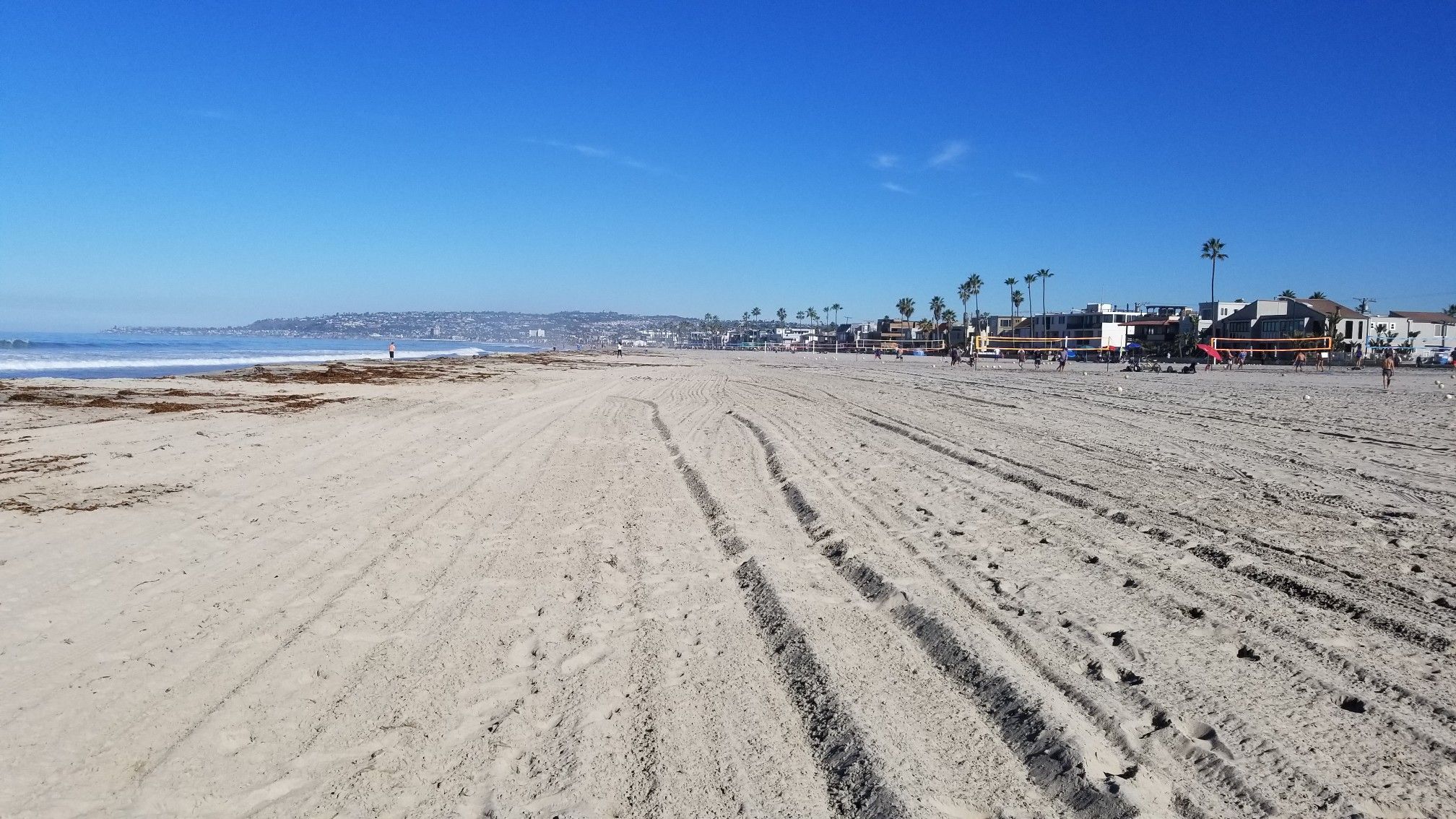 Vast sandy beach with tire tracks under a clear blue sky. - Ocean Front Walk
