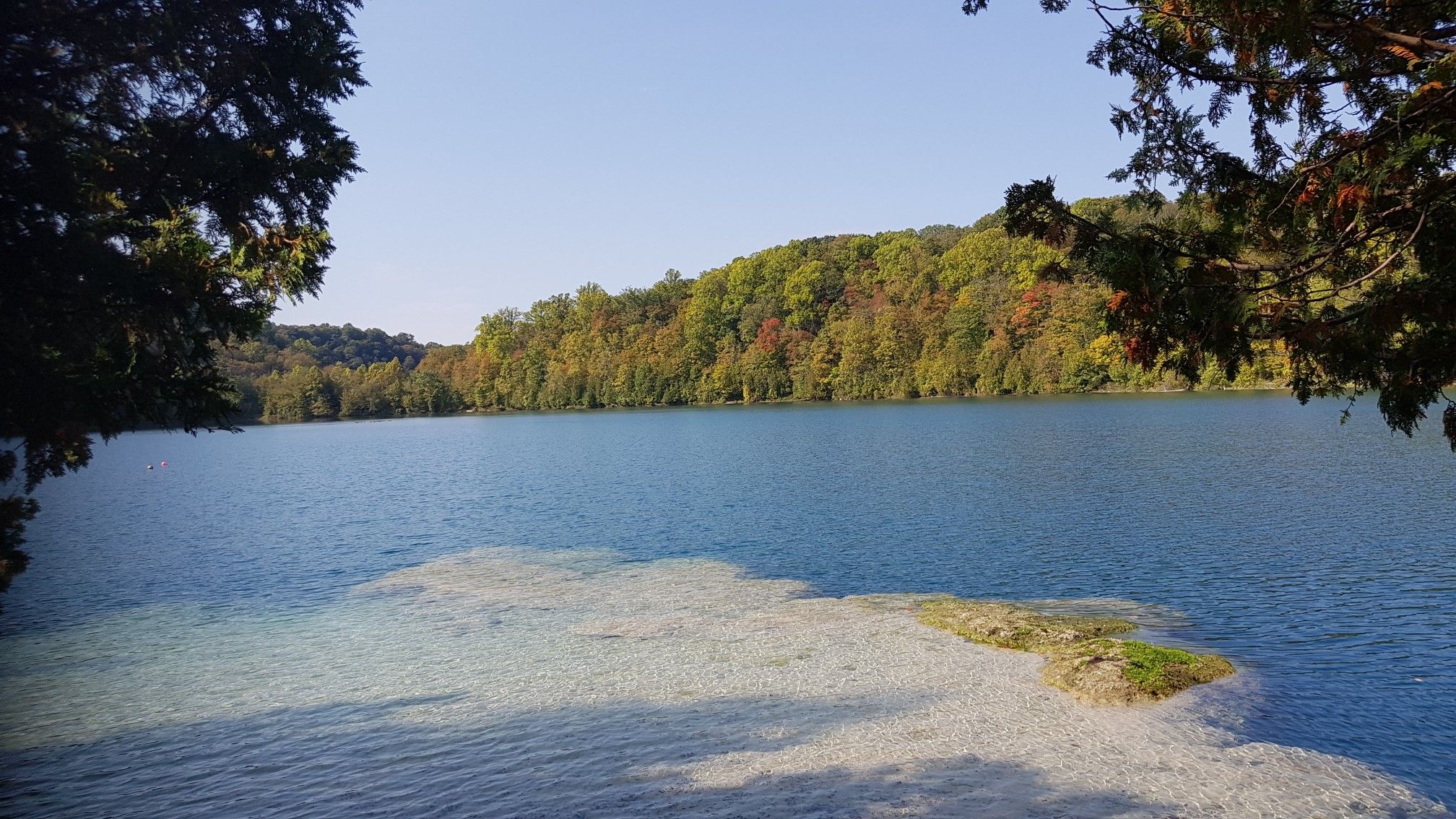 Clear lake with light-colored shallow areas, framed by green trees. - Round Lake loop from Green Lakes State Park