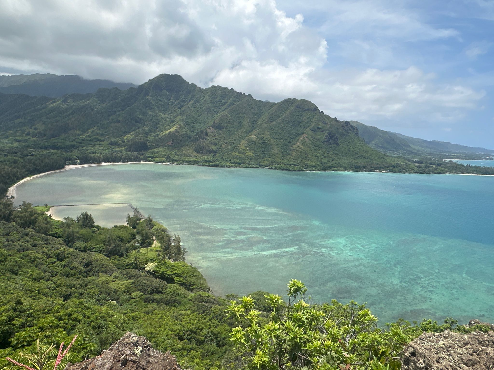 Expansive view of a turquoise bay, lush green mountains, and cloudy sky. - Puʻu Manamana Trail