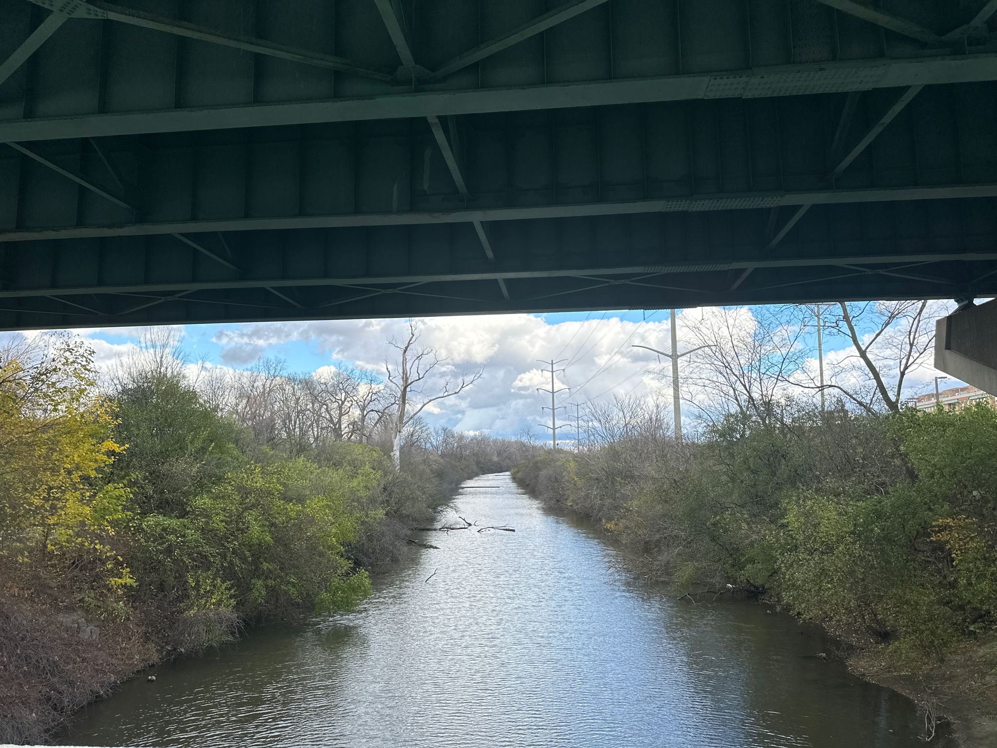 A view of a narrow canal from under a bridge, with distant trees and power lines. - Bike loop from Willow Springs
