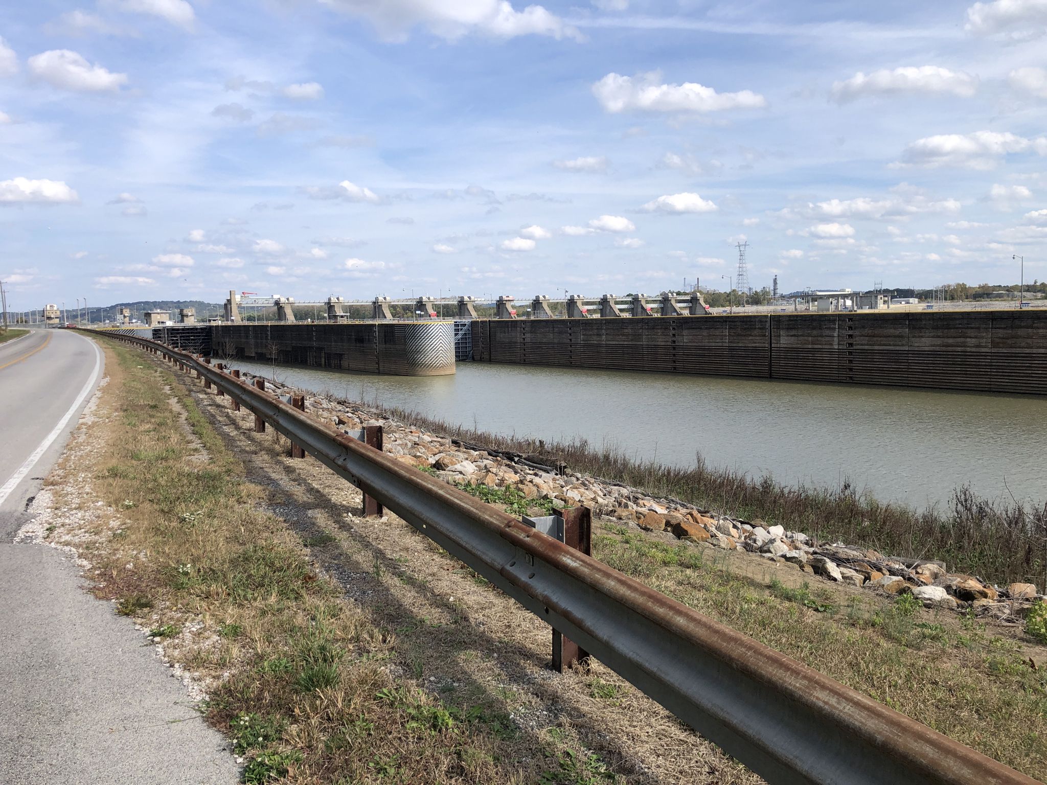 A long dam and waterway beside a road under a partly cloudy sky. - Cannelton loop
