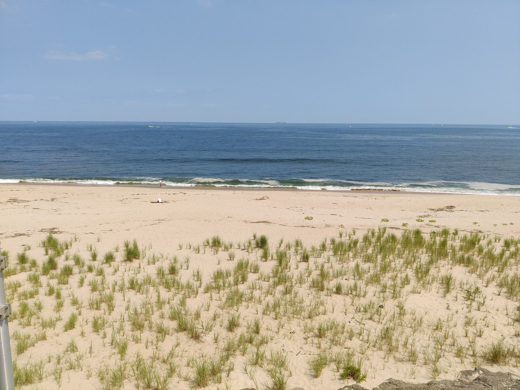 Wide sandy beach with sparse grass leading to the blue ocean. - Sandy Hook Multi-Use Path