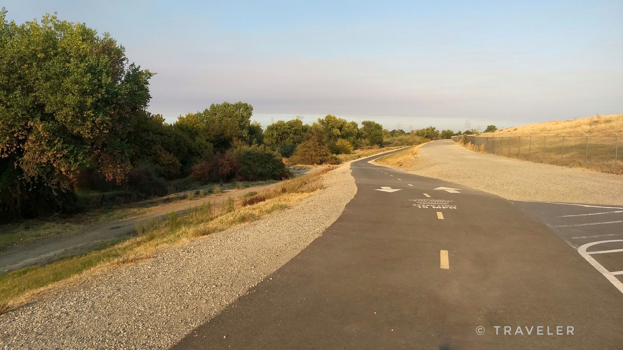Paved and gravel paths wind through a natural landscape at sunset. - Levee Path