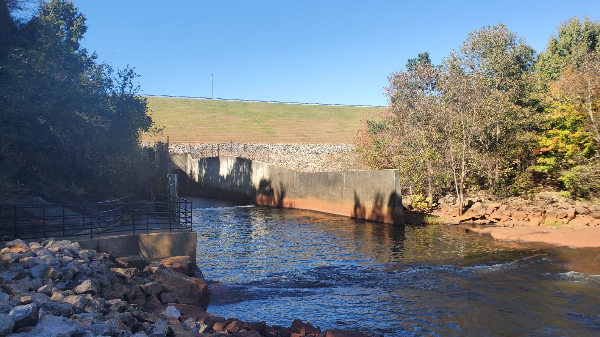 River flowing past concrete structures and autumn trees under a clear sky. - Long Leaf and Falls Lake Loop