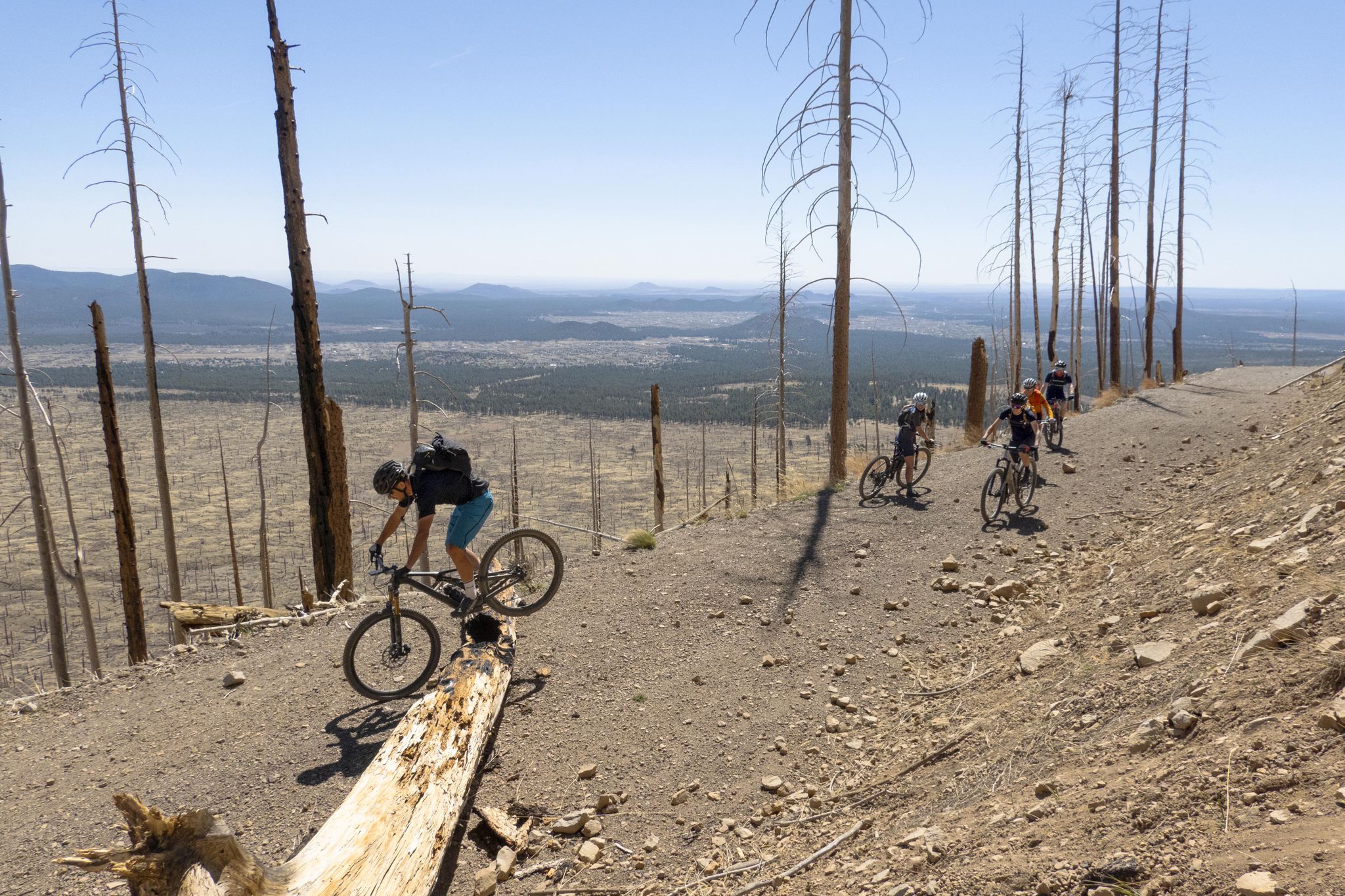 Group mountain biking down a dry, treeless hillside on a bright day. - Lockett Meadow via Waterline Road