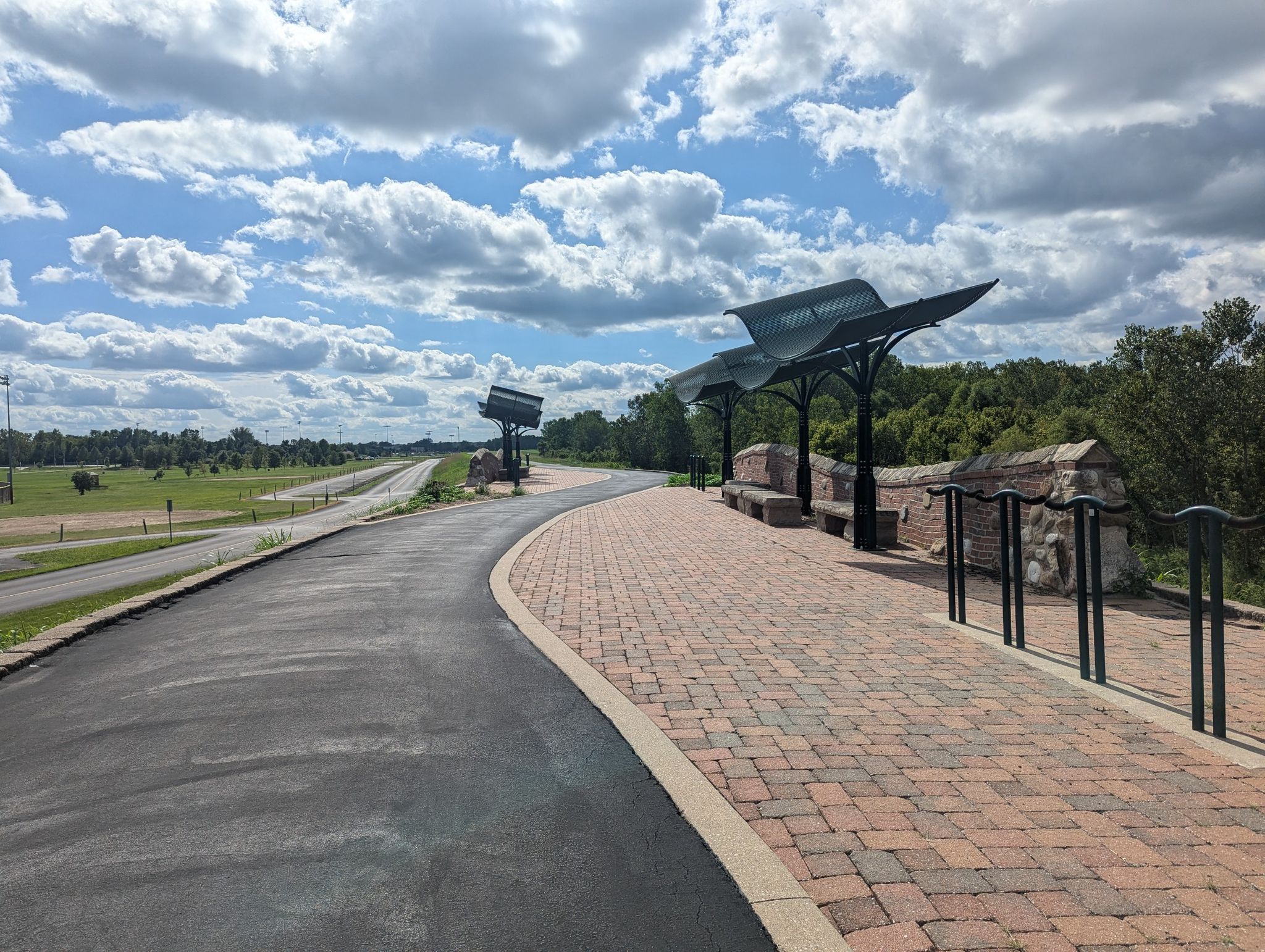 A paved path and brick plaza with modern shelters under a cloudy sky. - Chesterfield Settlers Cemetery loop from Chesterfield Airport at RHL
